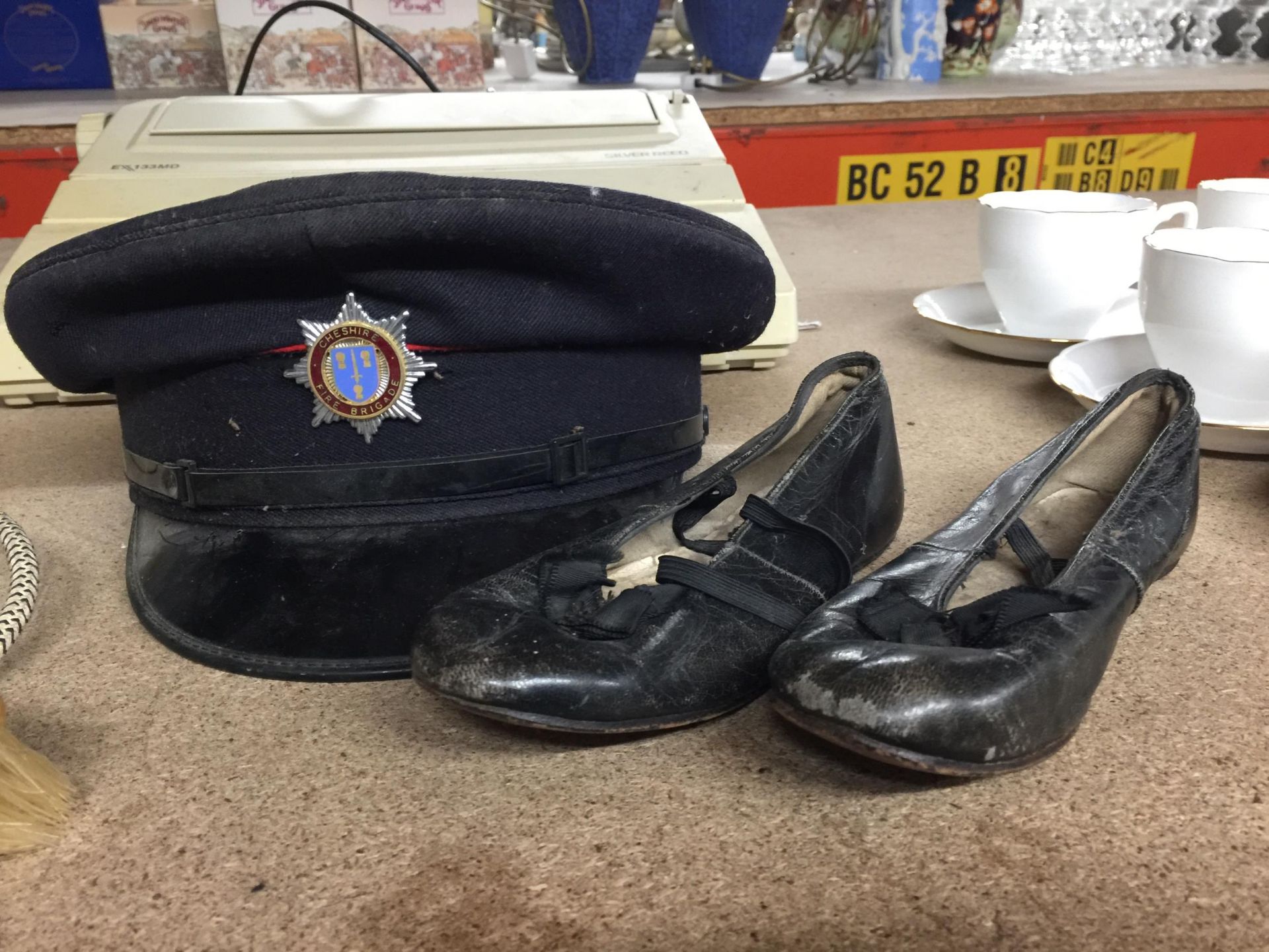 A VINTAGE CHESHIRE FIRE BRIGADE CAP WITH ORIGINAL BADGE AND A VINTAGE PAIR OF BALLET SHOES