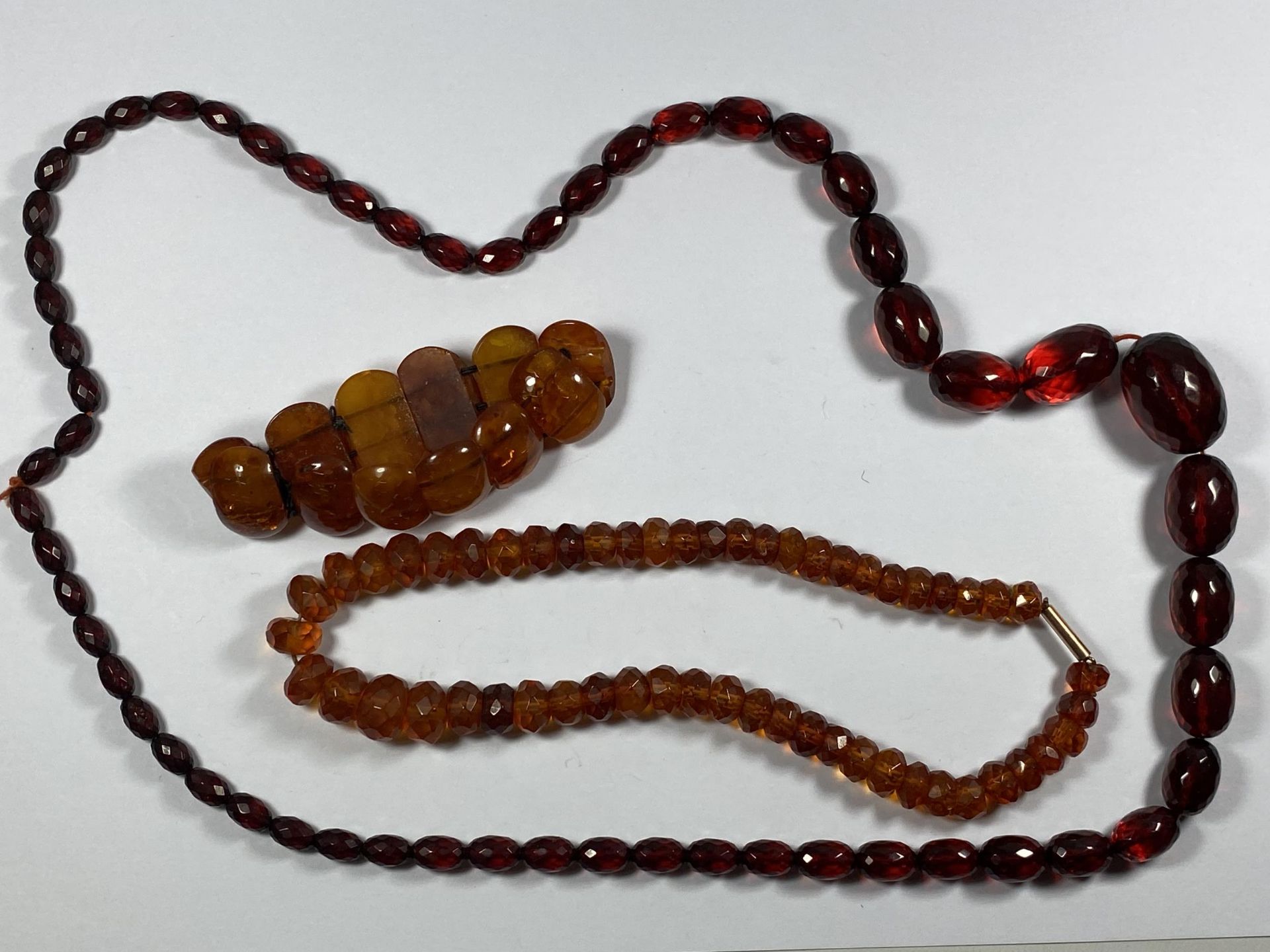 THREE BEADED ITEMS - RED GLASS NECKLACE, AMBER EFFECT BRACELET AND NECKLACE
