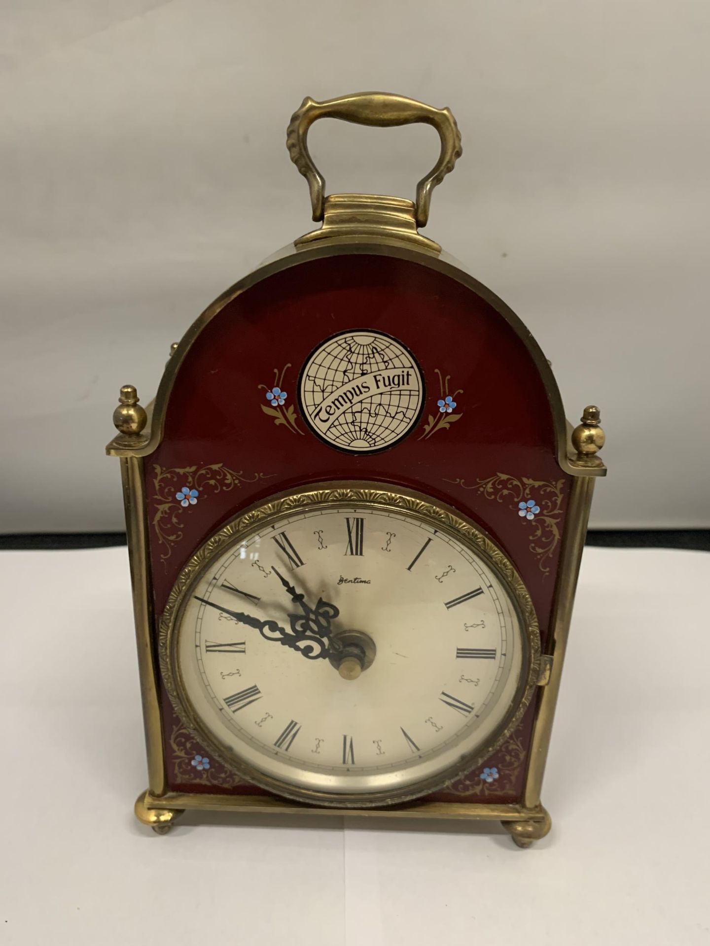 A 'BENTIMA' BRASS MANTLE CLOCK WITH A BURGUNDY AND FLORAL DECORATED FRONT HEIGHT 18CM