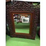 A 20TH CENTURY HARDWOOD WALL MIRROR WITH CARVED FOLIATE AND ANIMAL AND BIRD DECORATION 69CM X 56CM