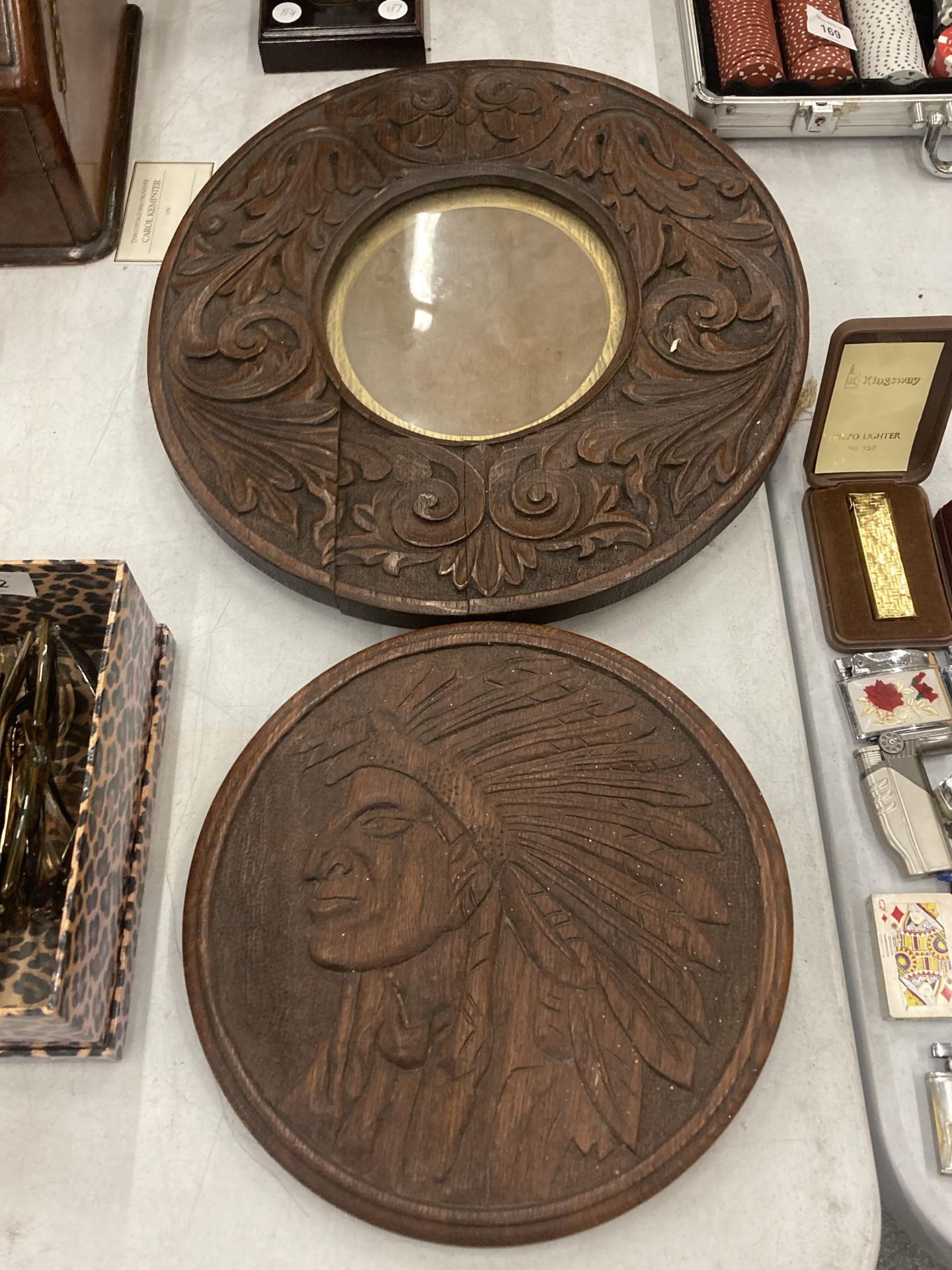 A WOODEN PLAQUE CARVED WITH A RED INDIAN AND A ROUND CARVED PICTURE FRAME