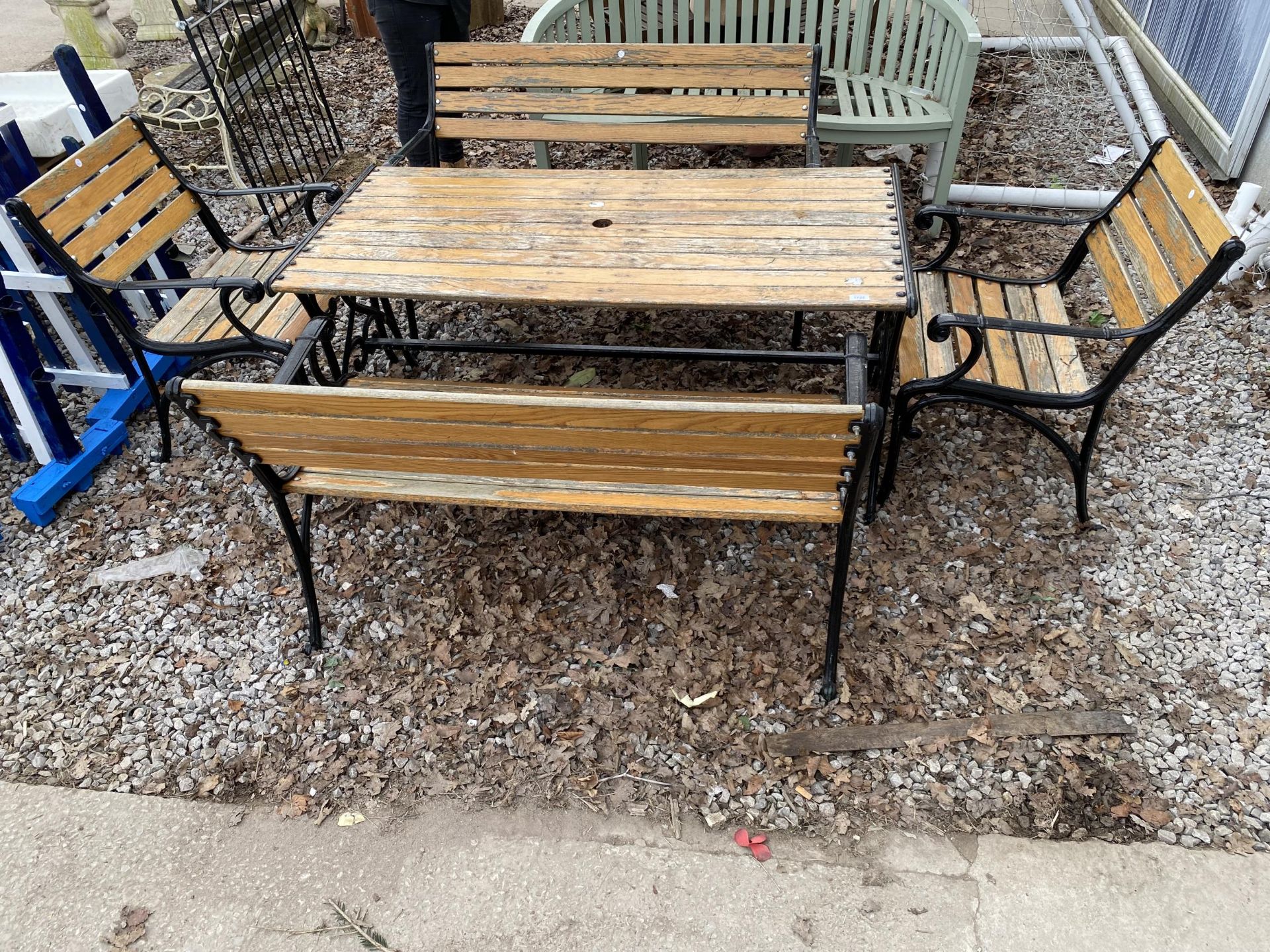 A WOODEN SLATTED PATIO FURNITURE SET WITH CAST TABLE BASE, TWO BENCHES AND TWO CHAIRS WITH CAST ENDS