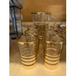 A LEMONADE SET WITH A JUG AND SIX GLASSES WITH A STRIPY GOLD COLOURED PATTERN