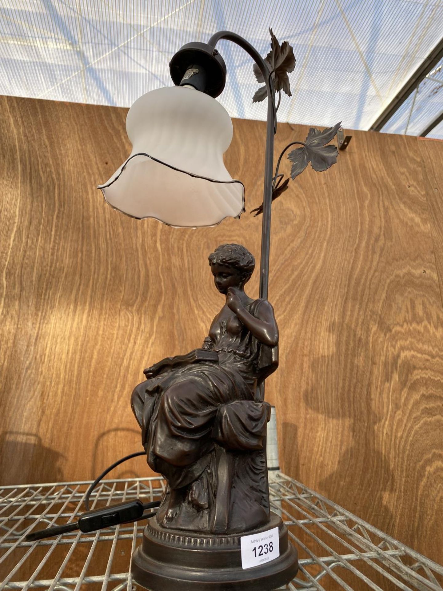 A METAL TABLE LAMP IN THE FORM OF A LADY READING A BOOK WITH A WHITE GLASS SHADE