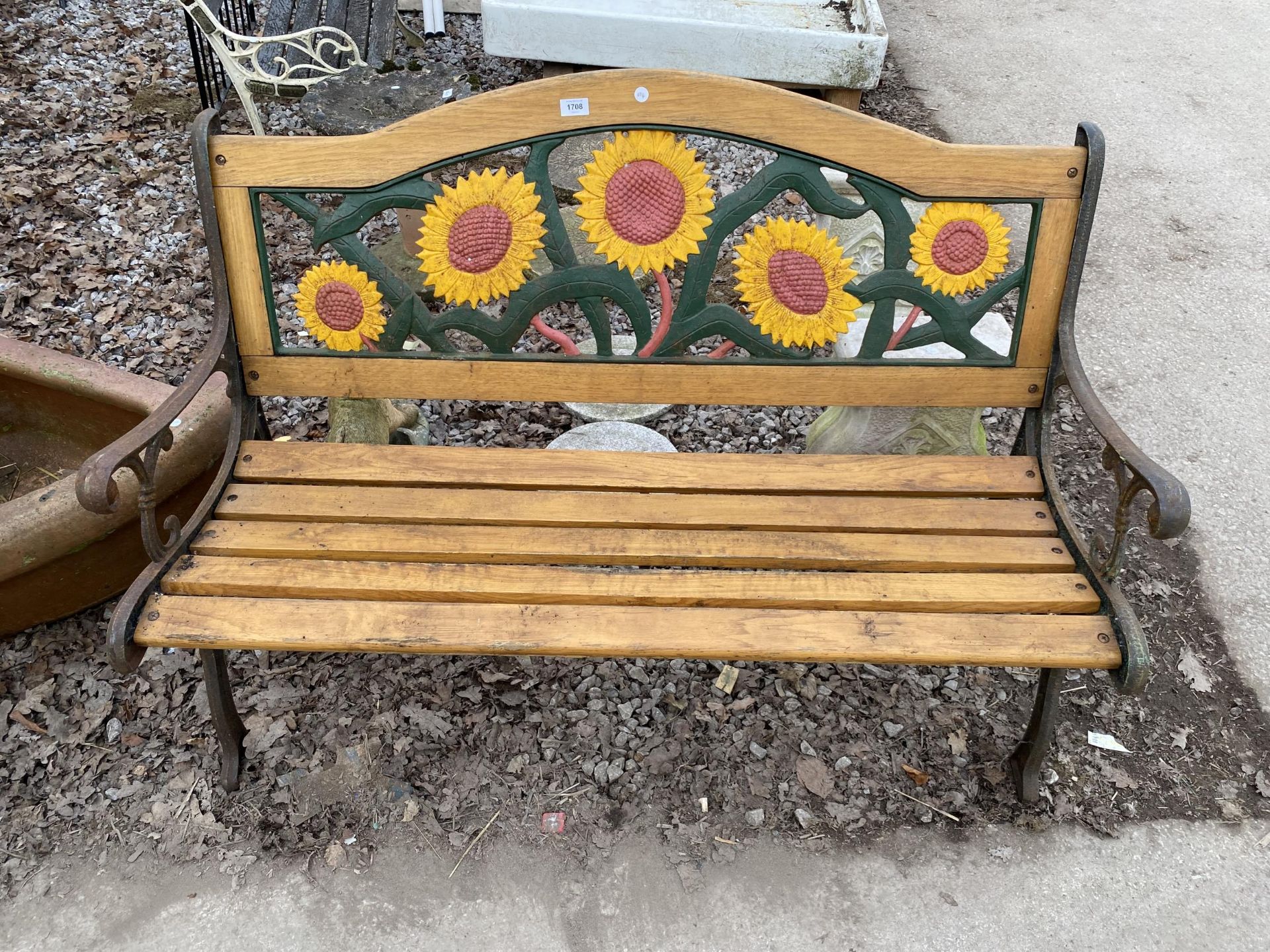 A WOODEN SLATTED GARDEN BENCH WITH CAST BENCH ENDS AND CAST SUNFLOWER DESIGN BACK