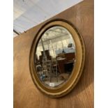 AN OVAL GILT FRAMED BEVELED EDGE WALL MIRROR