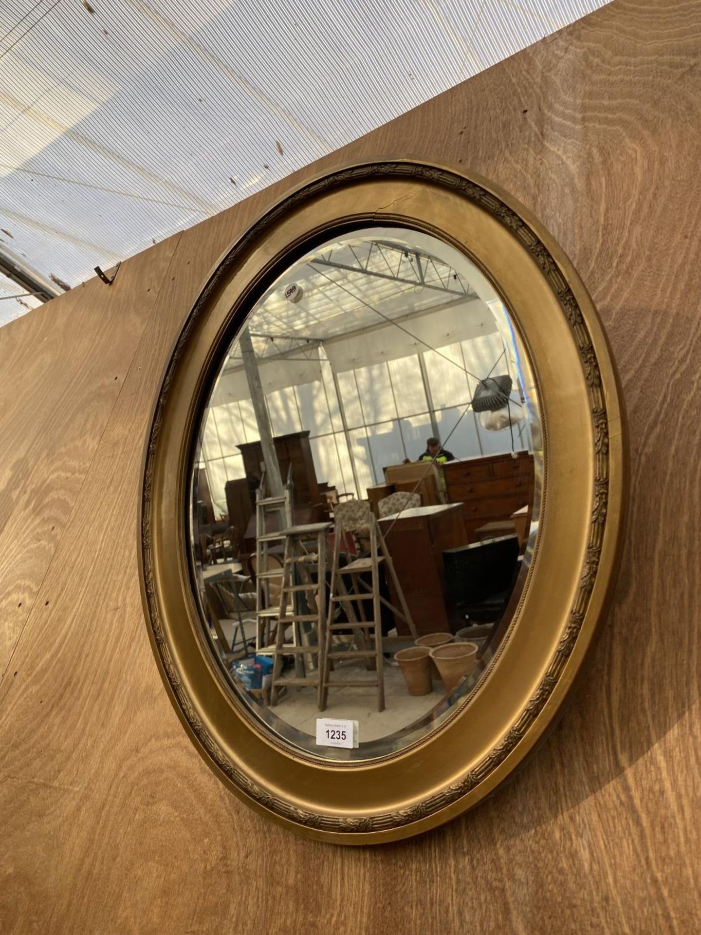 AN OVAL GILT FRAMED BEVELED EDGE WALL MIRROR