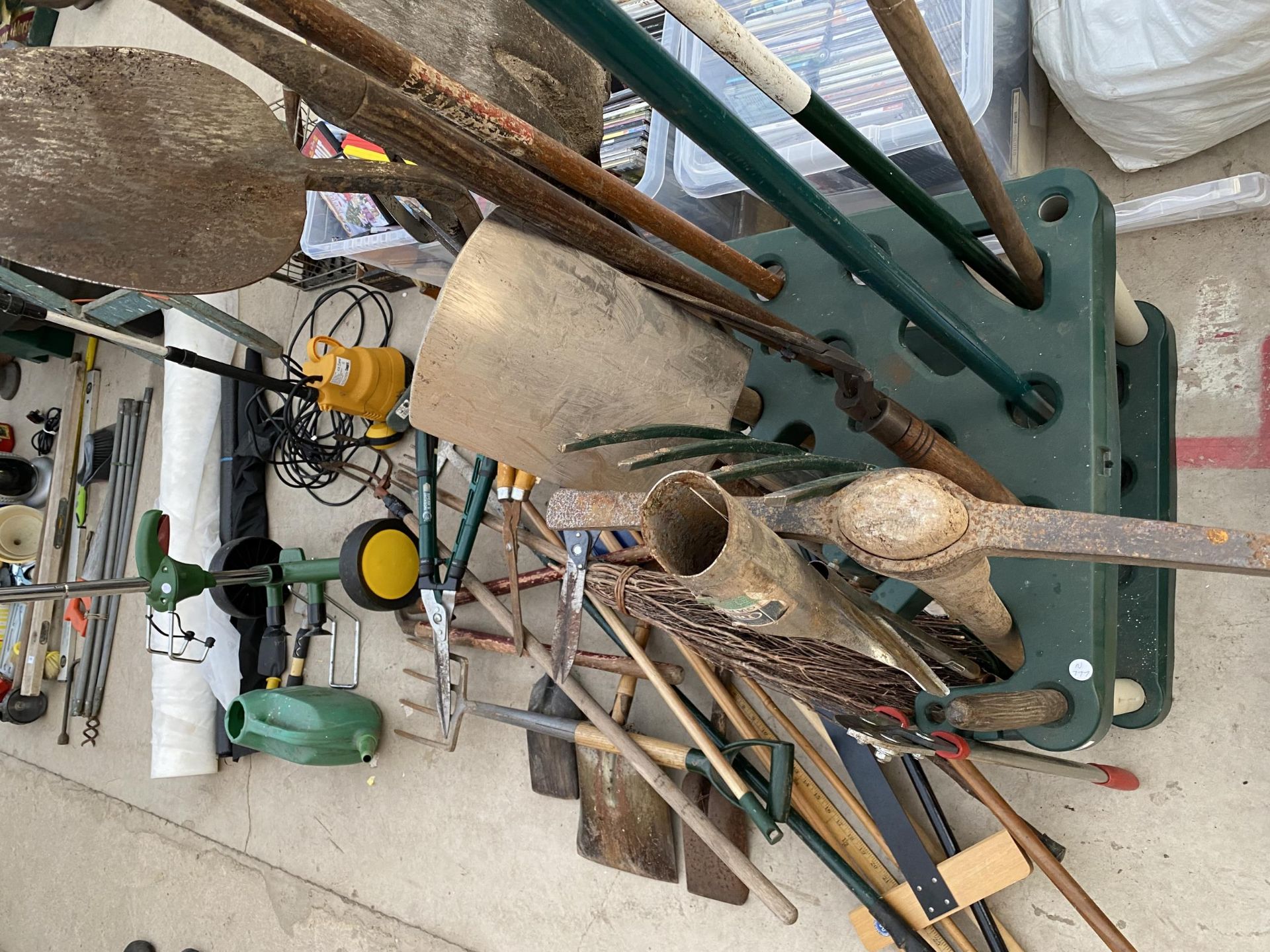A LARGE ASSORTMENT OF GARDEN TOOLS TO INCLUDE A PICK AXE, FORKS AND RAKES TO ALSO INCLUDE A PLANT