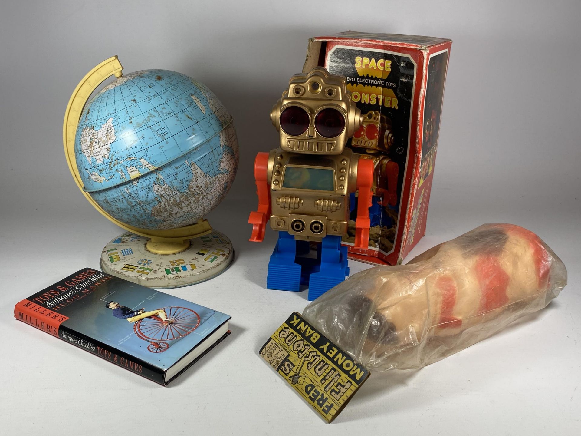 FOUR ITEMS - A BOXED ELECTRONIC SPACE MONSTER, PLASTIC FRED FLINTSTONE MONEY BANK, BOOK & TIN GLOBE