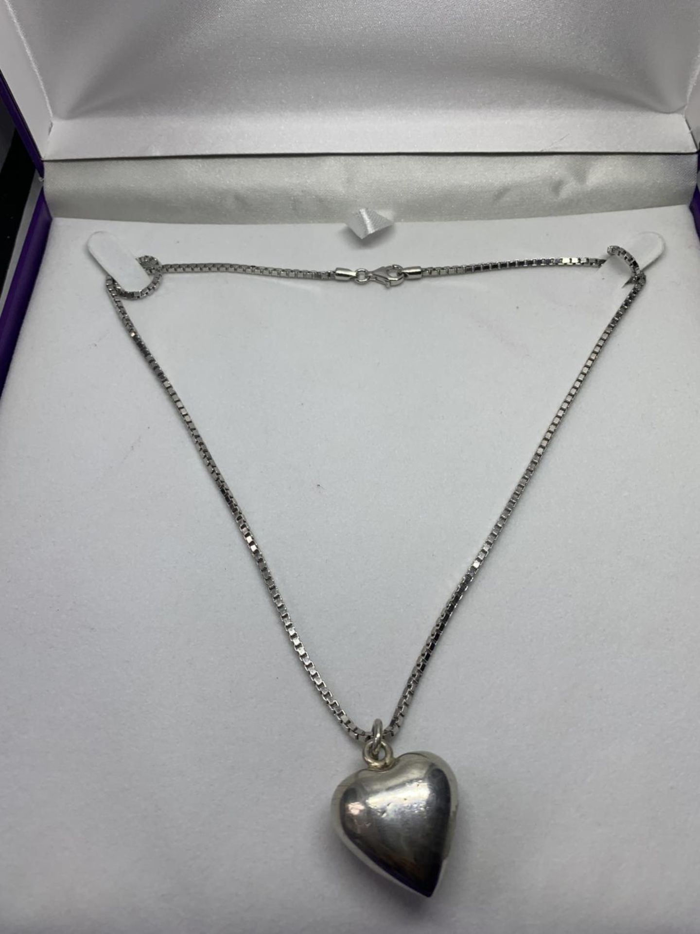 A SILVER NECKLACE WITH A HEART PENDANT IN A PRESENTATION BOX