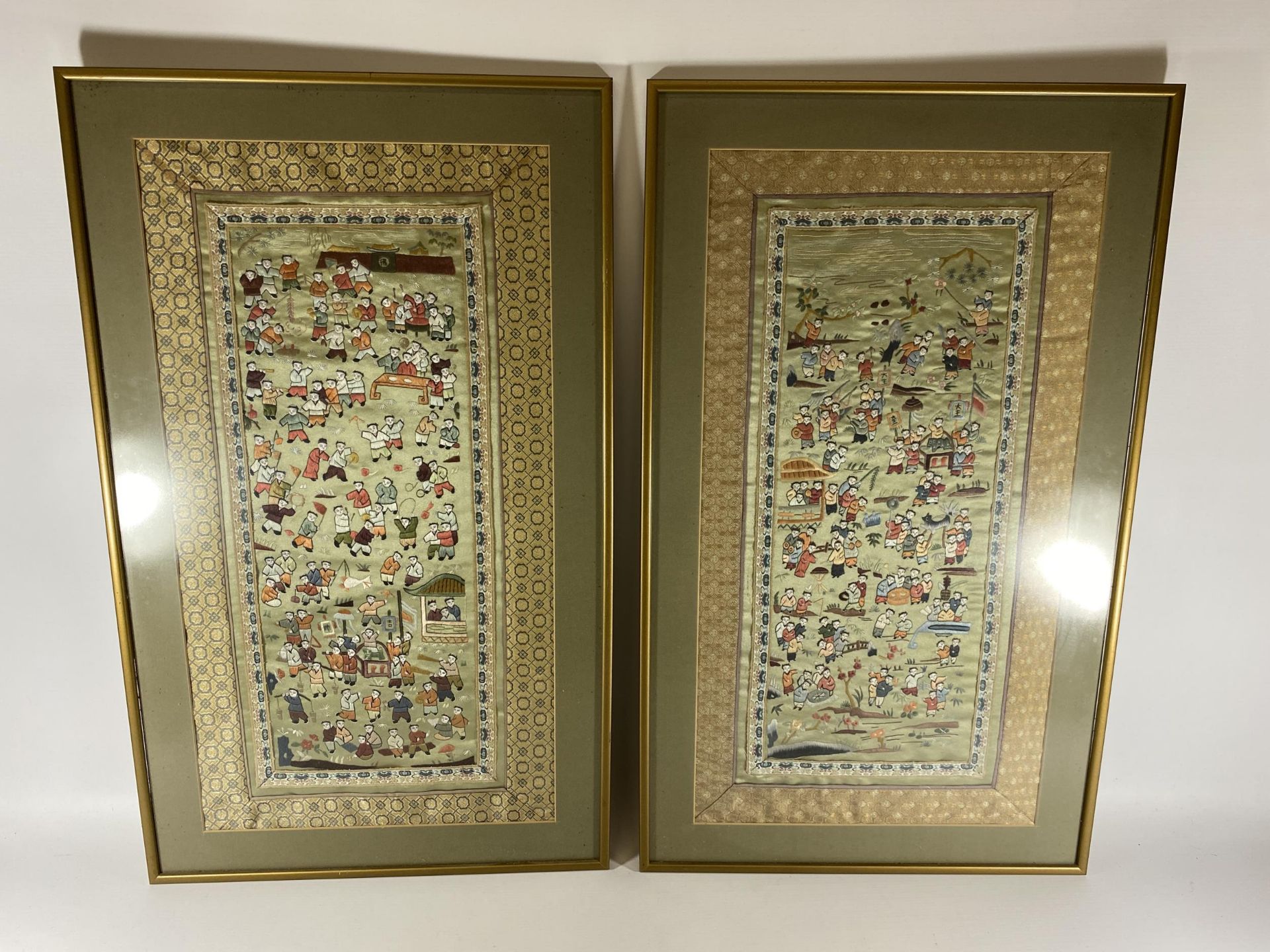 A PAIR OF GILT FRAMED CHINESE SILK PICTURES OF FIGURES ON A GREEN SILK GROUND, 71 X 43CM