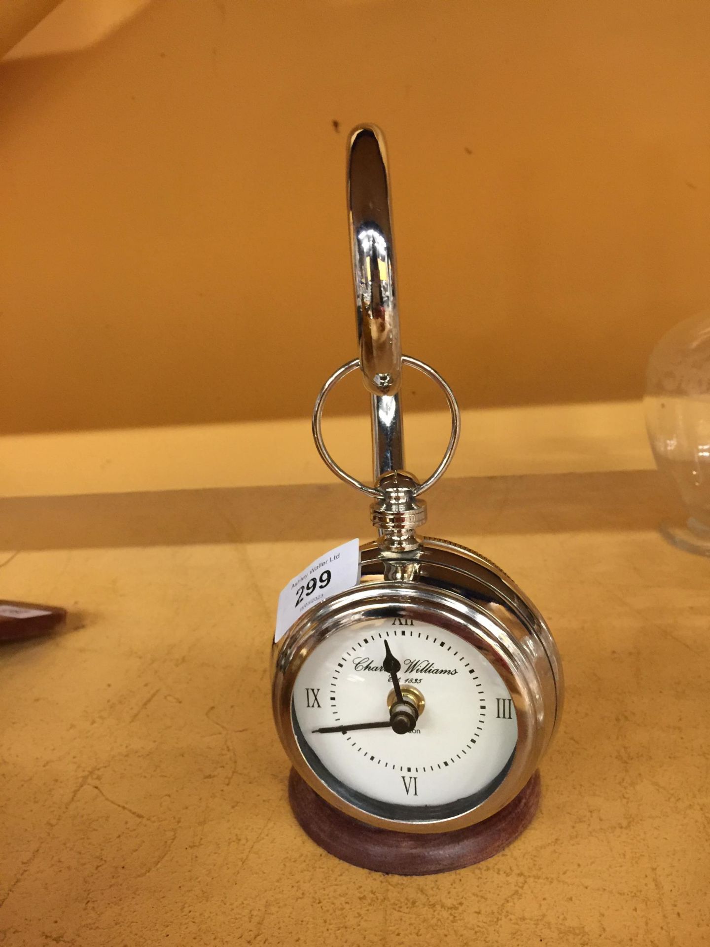 A CHROME POCKET WATCH STYLE CLOCK ON A CHROME STAND WITH WOODEN BASE