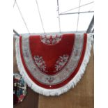 AN OVAL RED PATTERNED FRINGED RUG