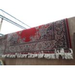 A LARGE RED PATTERNED FRINGED RUG