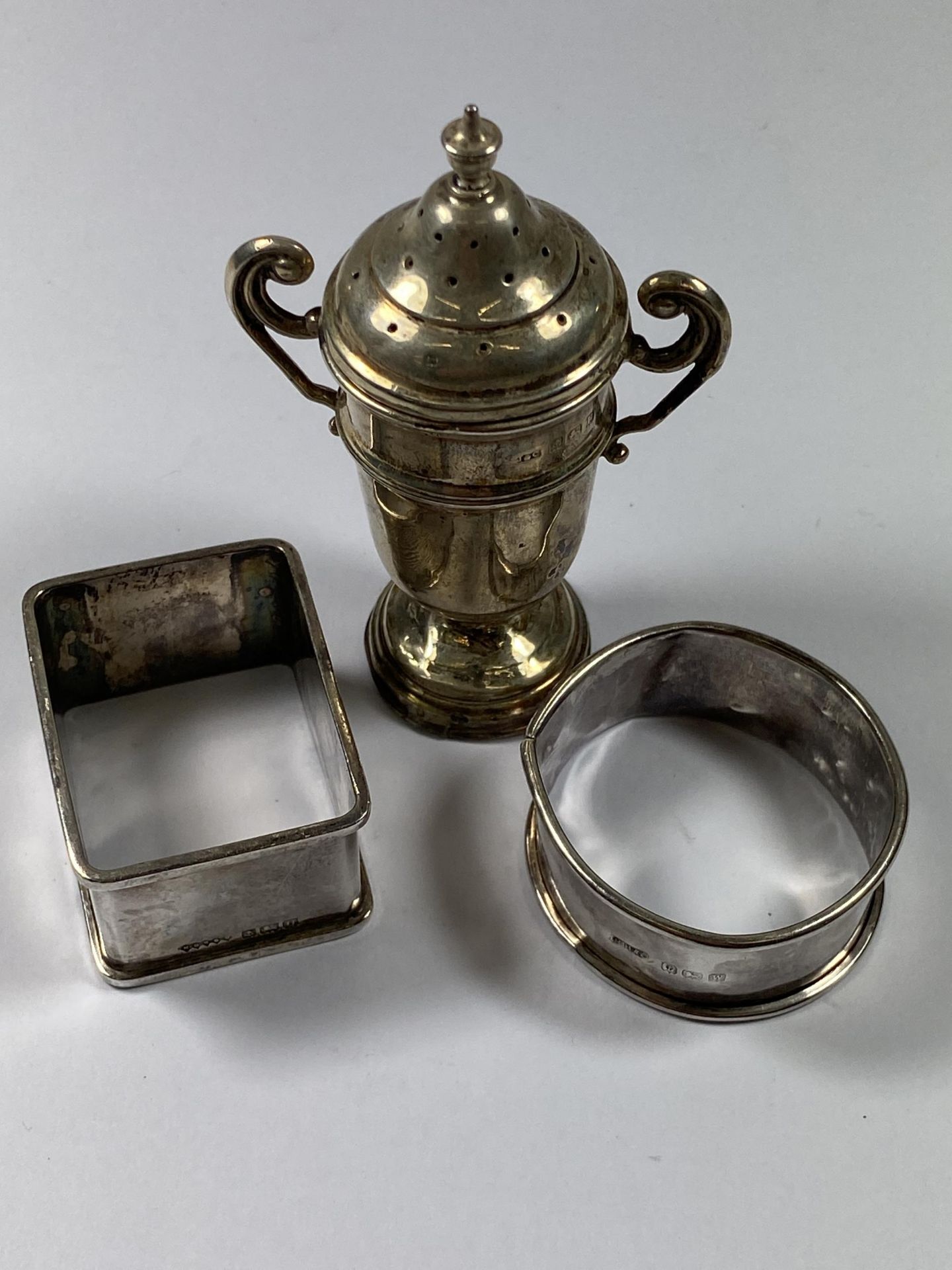 A GROUP OF THREE HALLMARKED SILVER ITEMS COMPRISING TWO NAPKIN RINGS AND A TWIN HANDLED SUGAR SHAKER