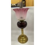 AN EARLY TO MID 20TH CENTURY BRASS CORINTHIAN COLUMN OIL LAMP WITH CRANBERRY GLASS SHADE