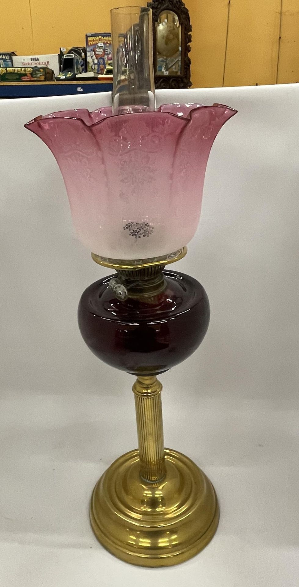 AN EARLY TO MID 20TH CENTURY BRASS CORINTHIAN COLUMN OIL LAMP WITH CRANBERRY GLASS SHADE