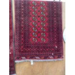 A RED PATTERNED FRINGED RUG (208CM x 102CM)