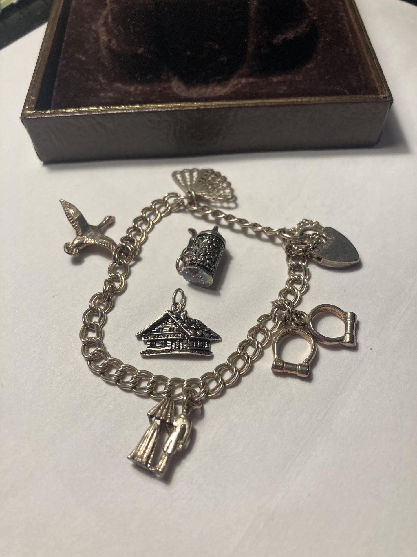 A SILVER CHARM BRACELET WITH SIX CHARMS AND A HALLMARKED BIRMINGHAM HEART PADLOCK