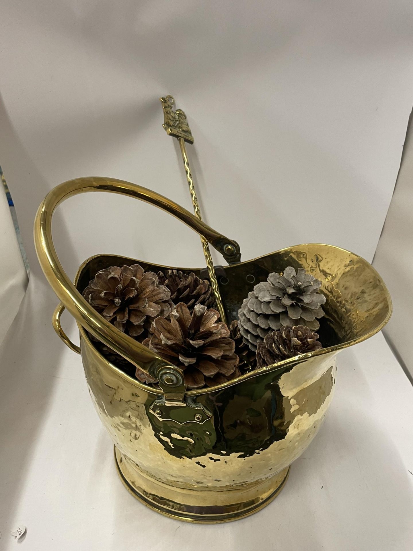 A VINTAGE HAMMERED EFFECT BRASS COAL BUCKET FILLED WITH PINE CONES