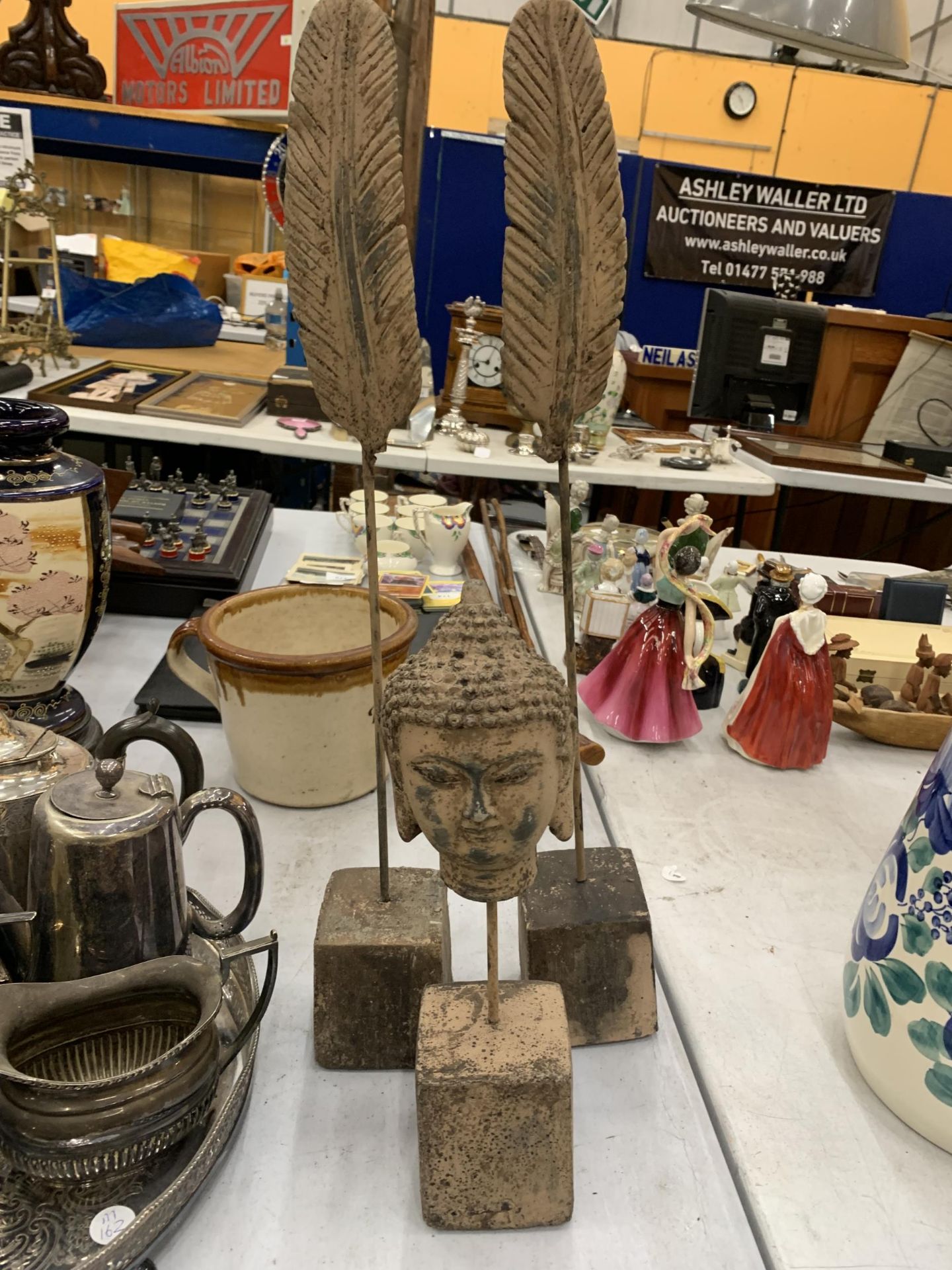 TWO STONE FEATHERS ON PLINTHS AND A BUDDAHS HEAD ON A PLINTH