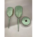 AN ART DECO HALLMARKED SILVER AND FLORAL GREEN ENAMEL THREE PIECE DRESSING SET