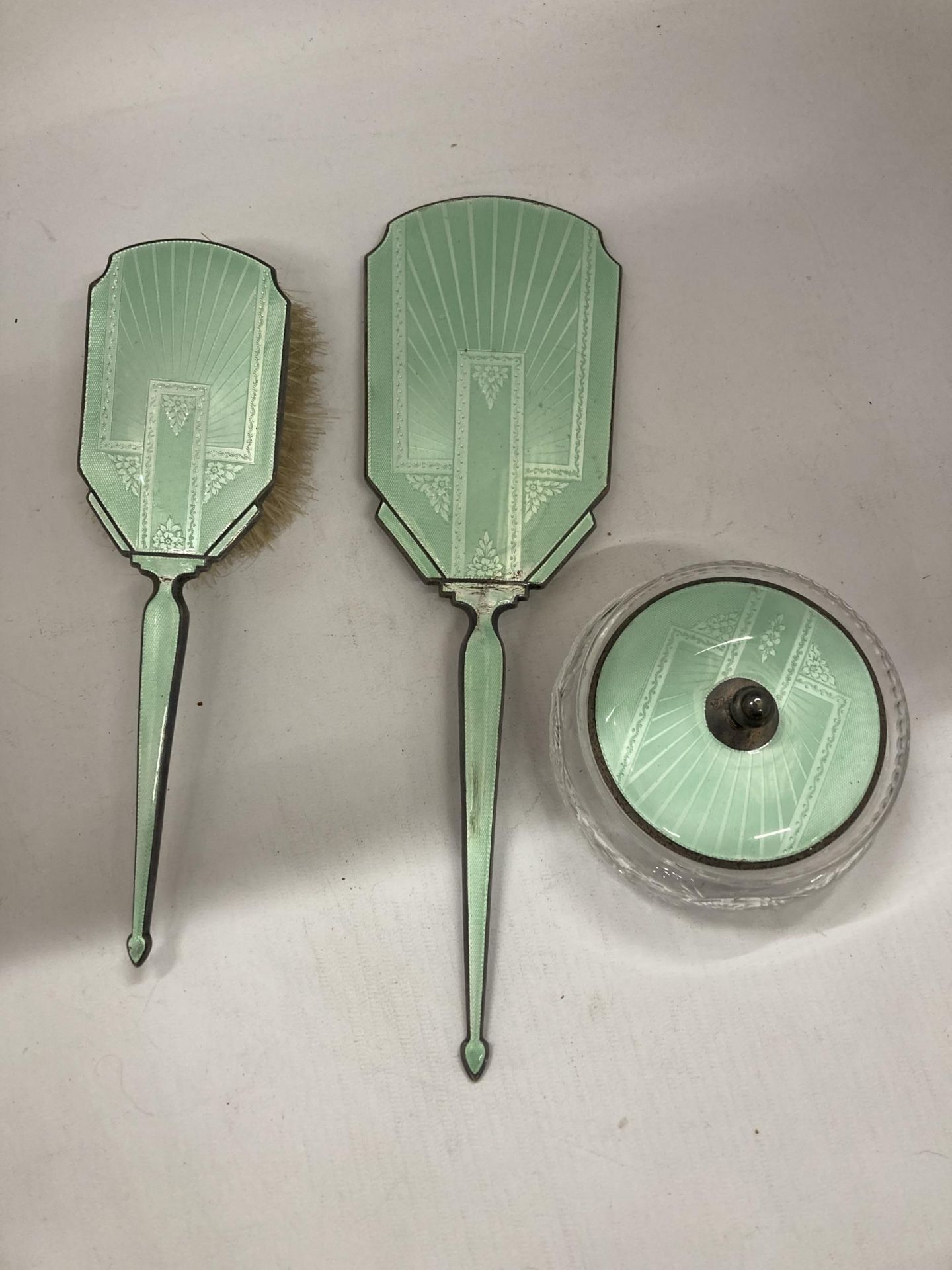 AN ART DECO HALLMARKED SILVER AND FLORAL GREEN ENAMEL THREE PIECE DRESSING SET