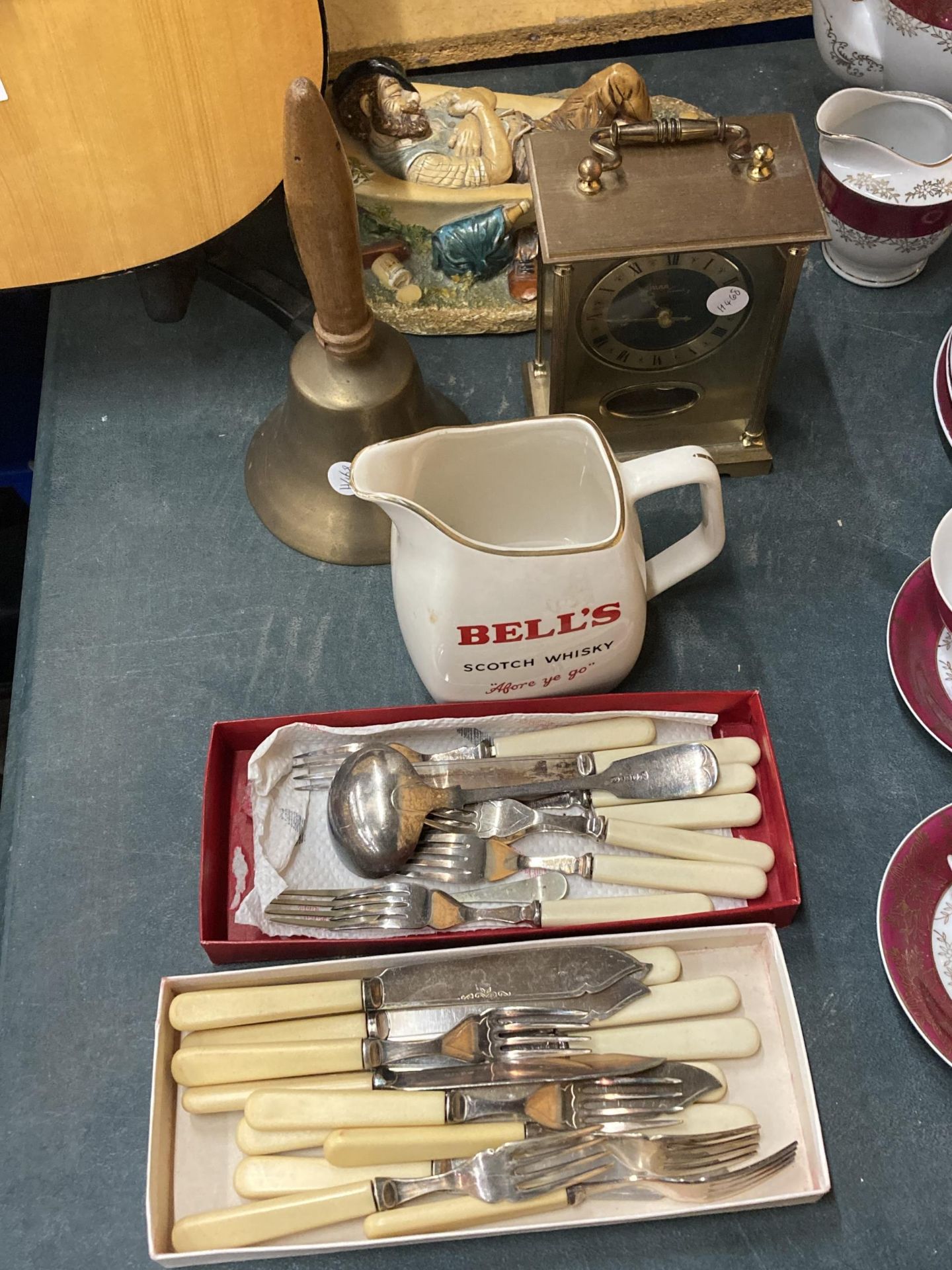 A MIXED LOT TO INCLUDE FLATWARE, A BELL'S WHISKY WATER JUG, BRASS BELL, FIGURE AND MANTLE CLOCK