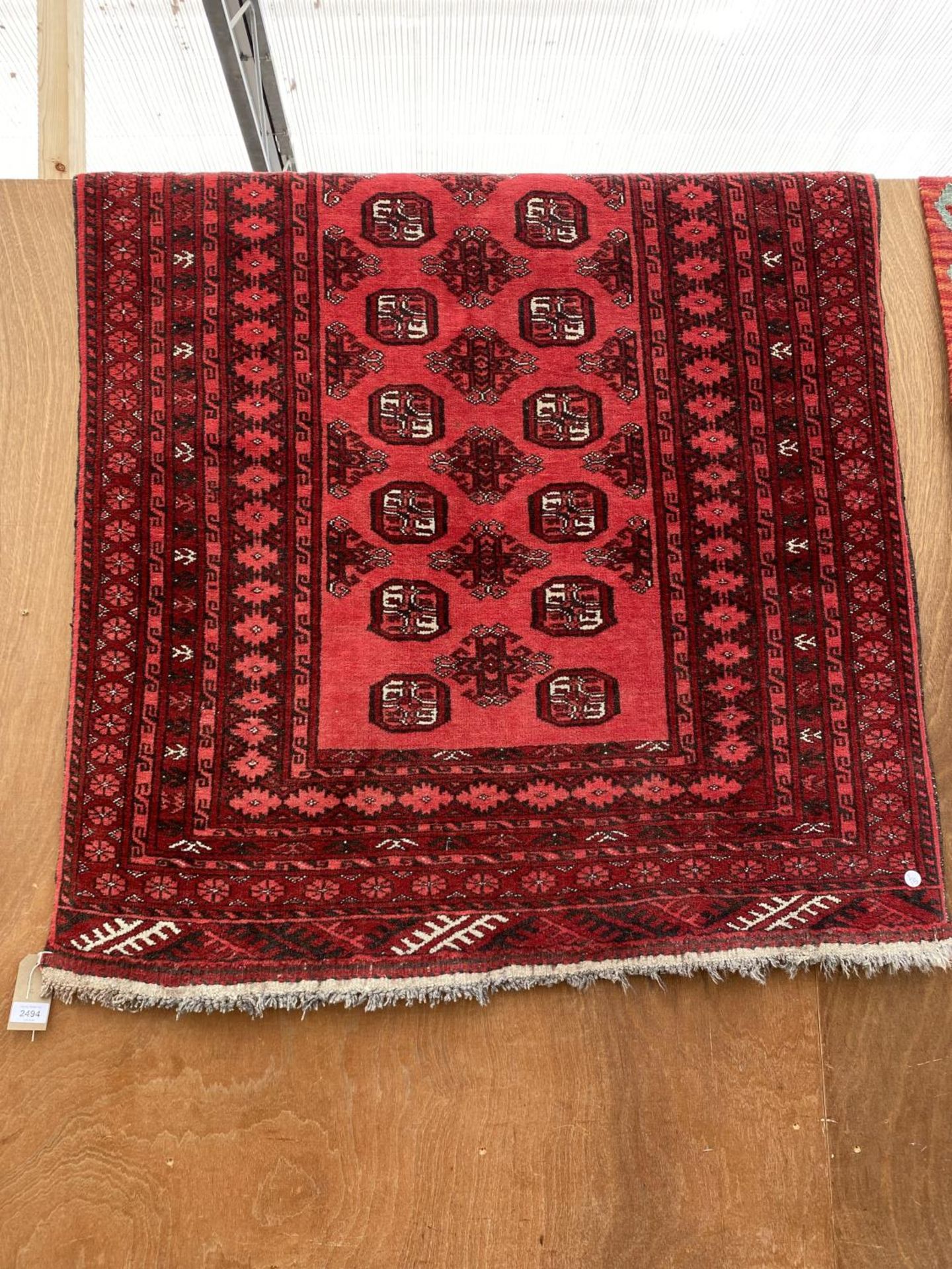 A RED PATTERNED FRINGED RUG (185CM x 107CM)