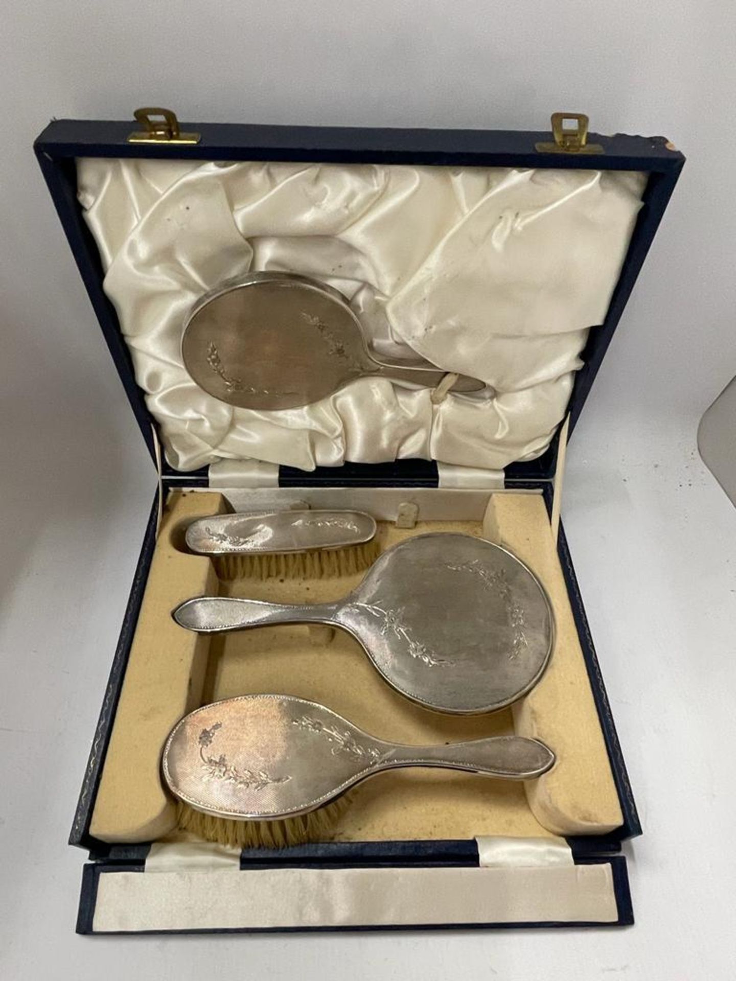 A CASED HALLMARKED SILVER BACKED FOUR PIECE DRESSING TABLE SET WITH FLORAL DESIGN