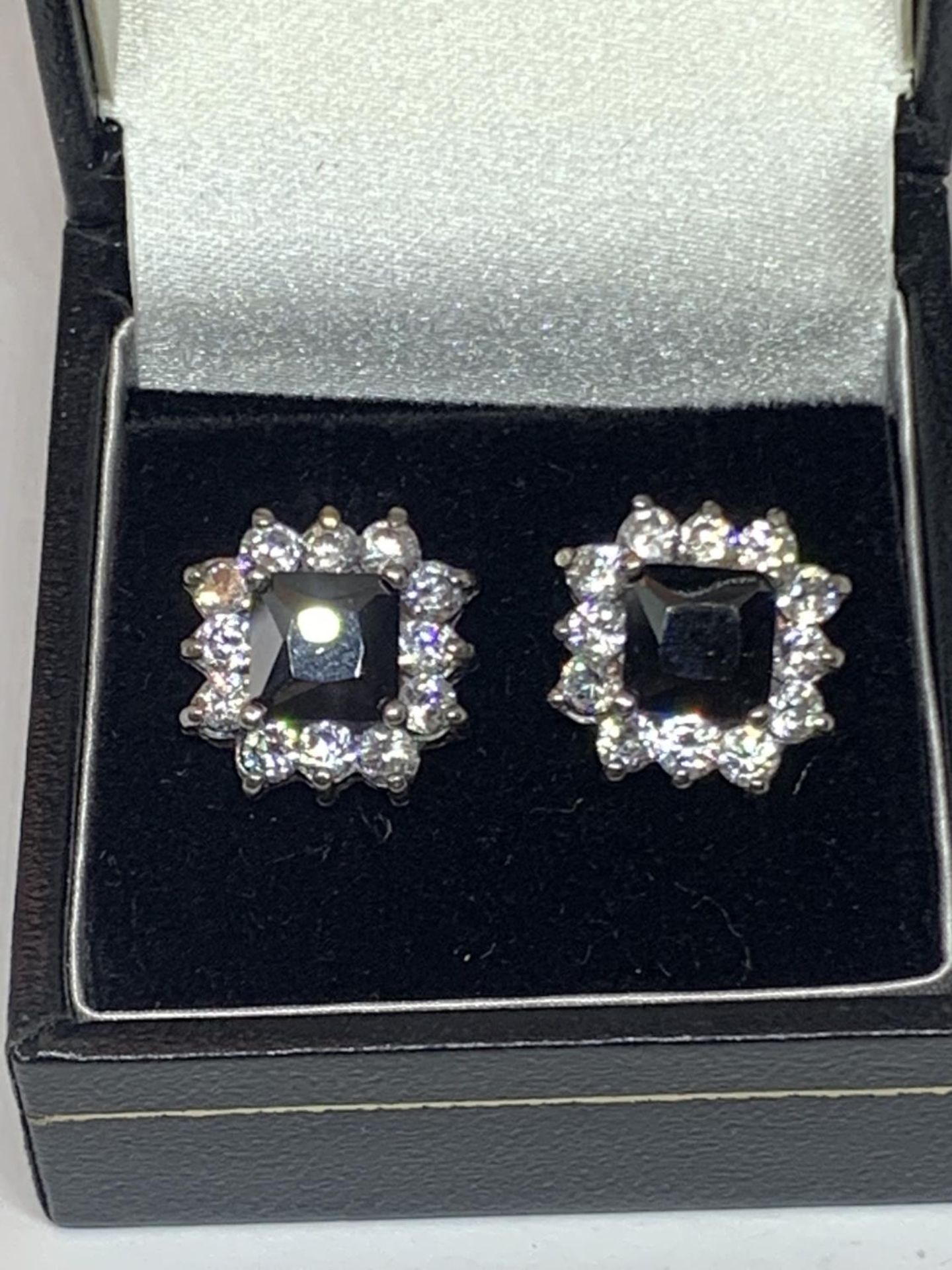 A PAIR OF SILVER EARRINGS WITH A DARK STONE SURROUNDED BY TWELVE CLEAR STONES IN A PRESENTATION BOX