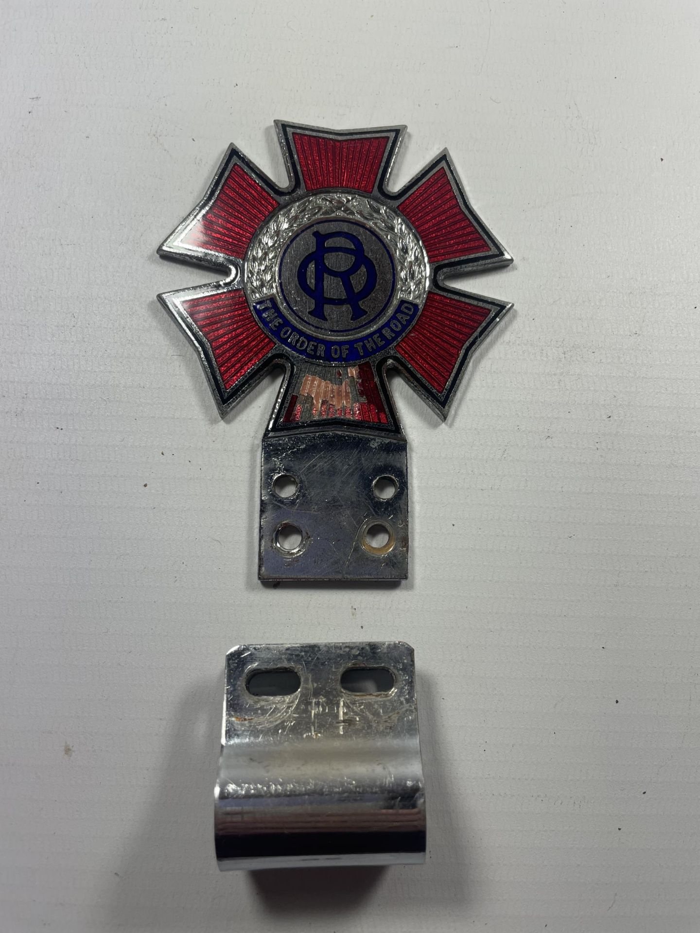 A VINTAGE ENAMEL ORDER OF THE ROAD BUMPER BADGE WITH CLIP