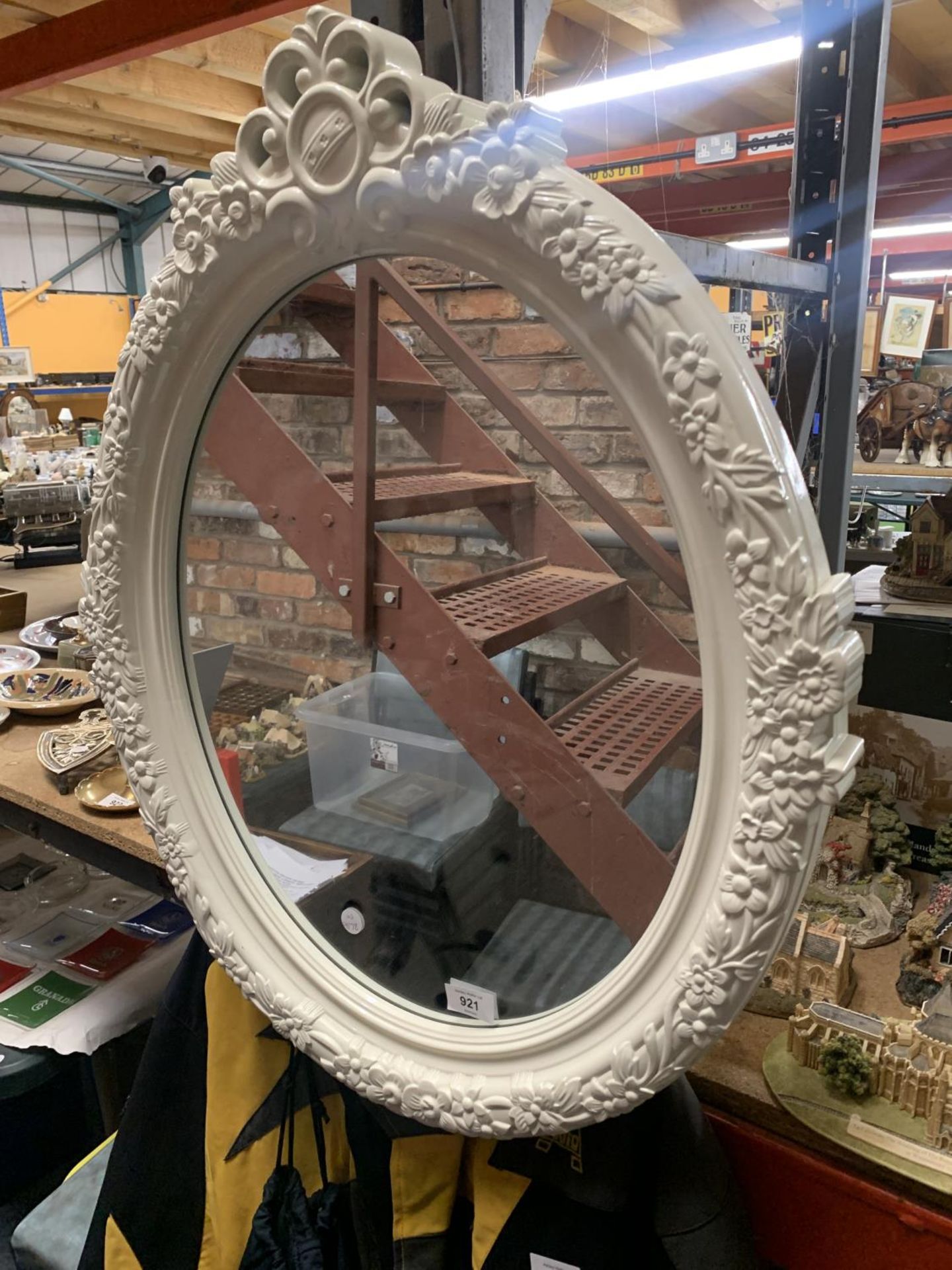 A MODERN OVAL WALL MIRROR WITH WHITE FLORAL SURROUND 56CM X 70CM