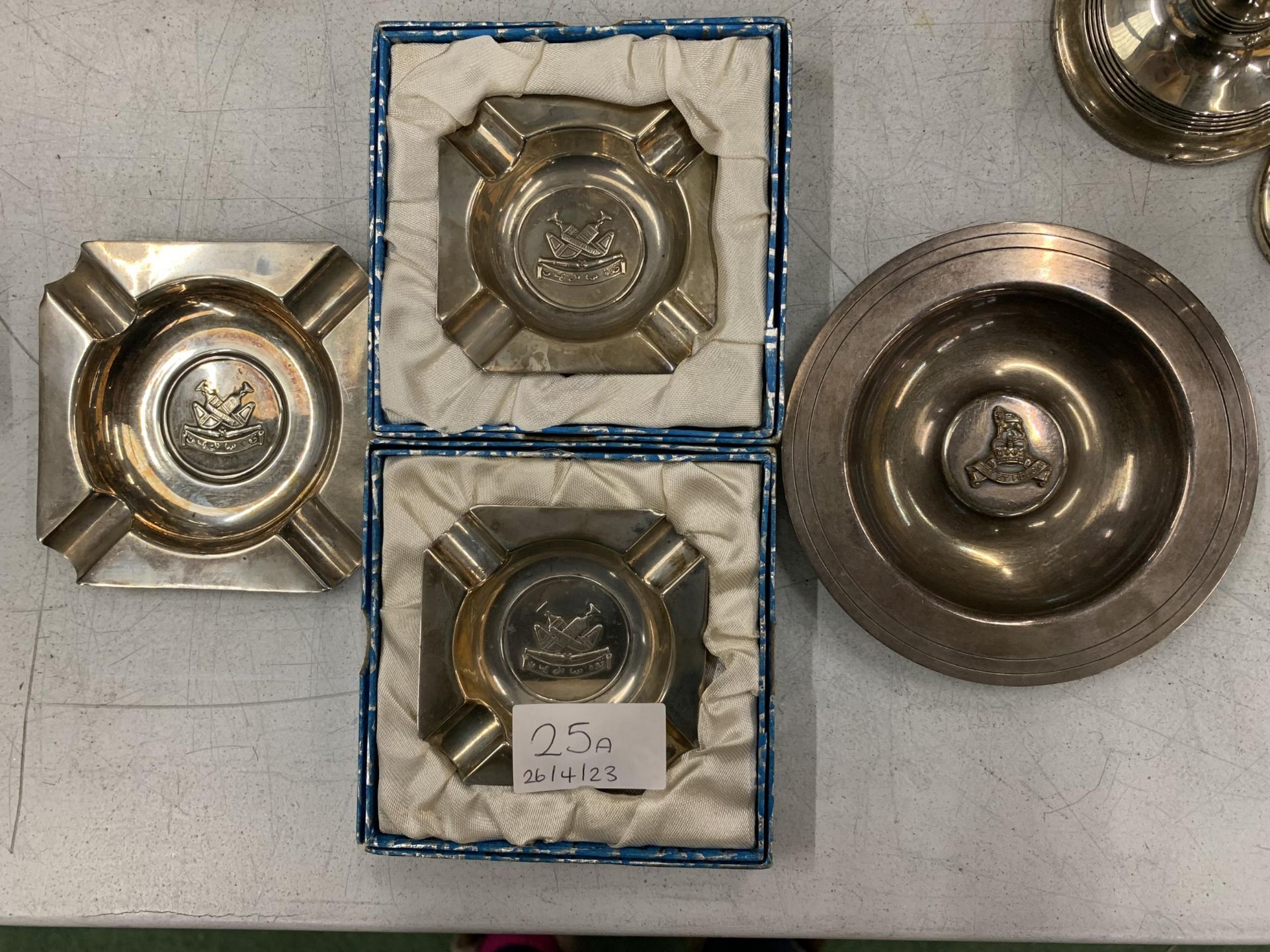 THREE SILVER PLUS ONE WHITE METAL ASHTRAYS WITH MILITARY EMBLEMS