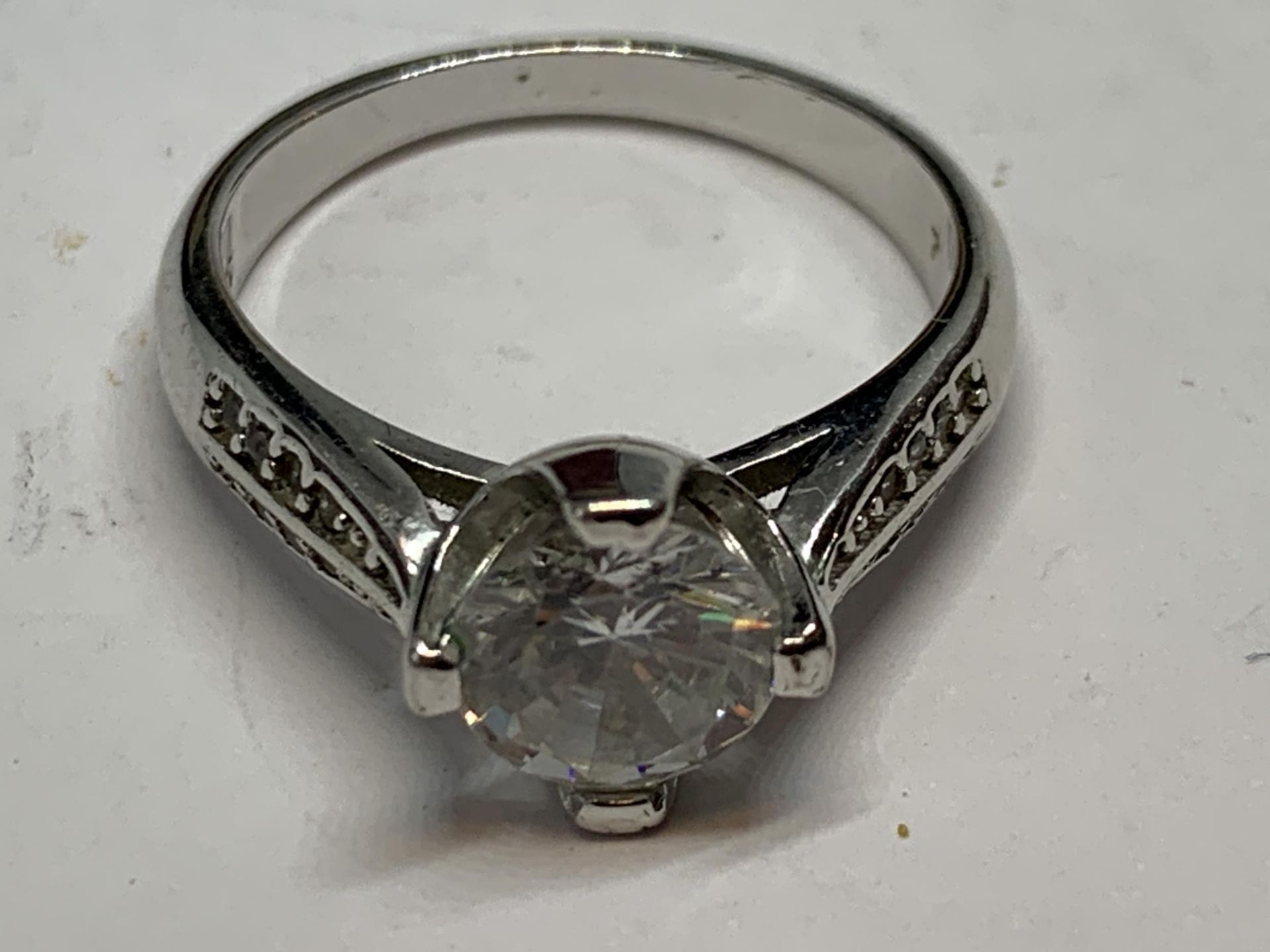 A SILVER RING WITH A LARGE SOLITAIRE CLEAR STONE AND CLEARSTONES TOO SHOULDERS SIZE M/N IN A