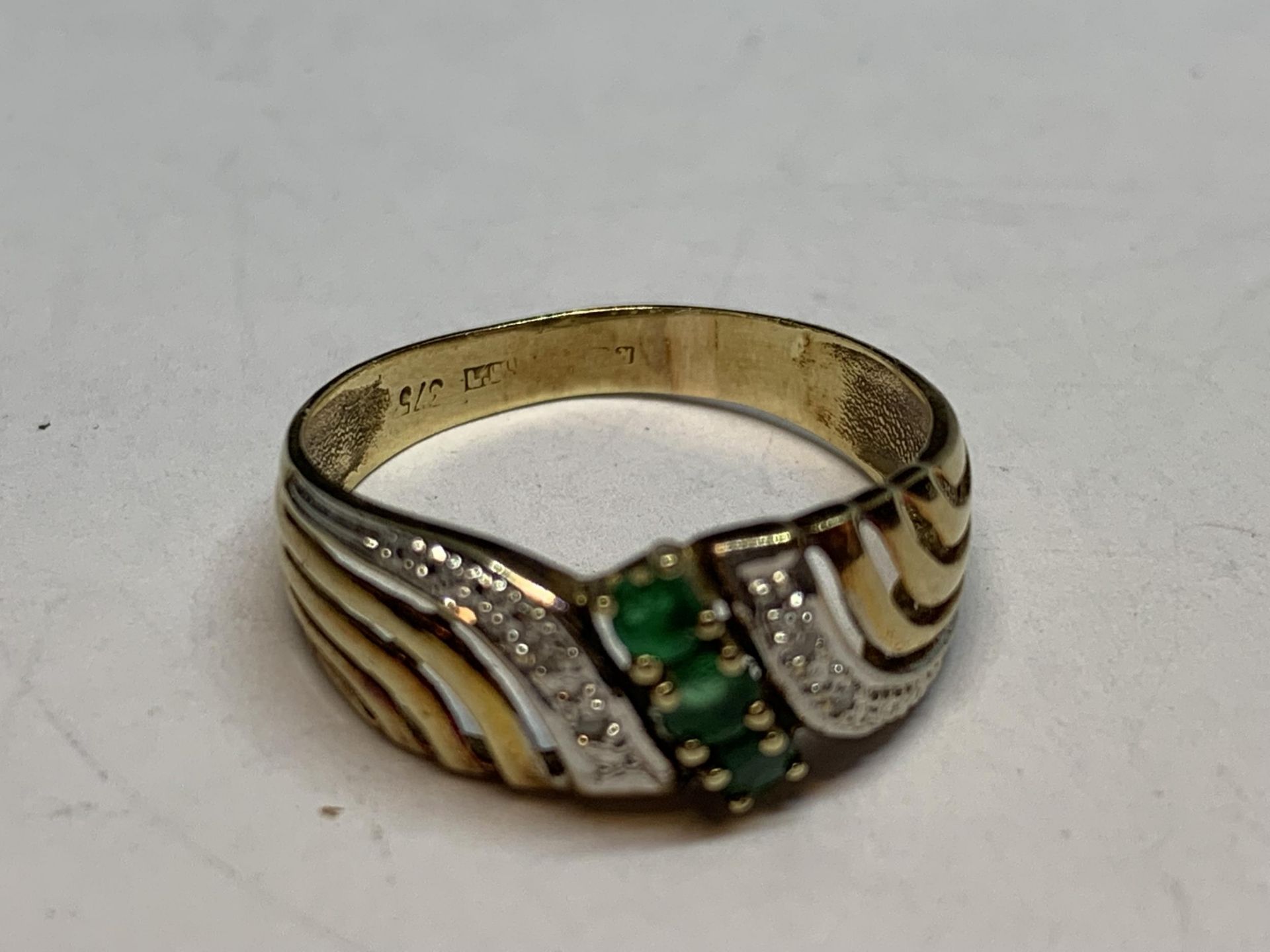 A 9 CARAT GOLD RING WITH THREE GREEN STONEES SORROUNDED BY CLEAR STONES GROSS WEIGHT 2 GRAMS SIZE P