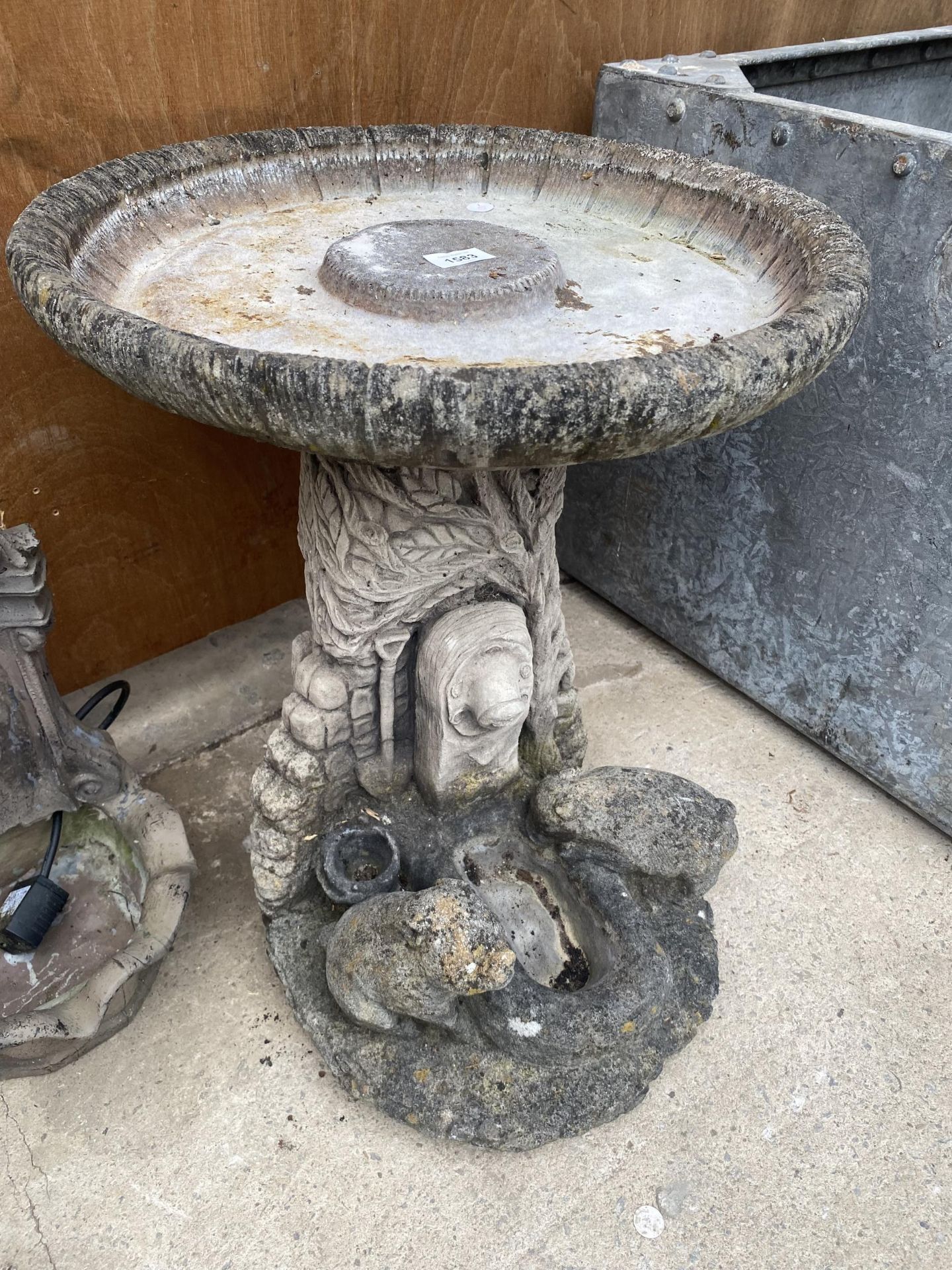 A RECONSTITUTED STONE BIRDBATH WITH PEDESTAL BASE FEATURING ANIMALS AT A TROUGH