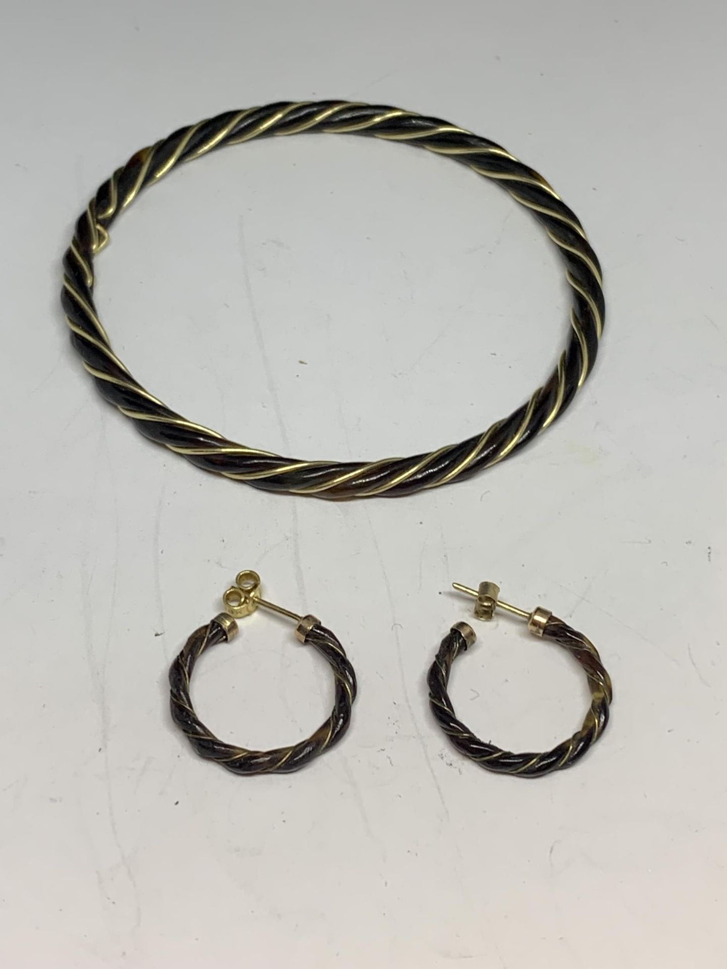 A BLACK BANGLE WITH A TESTED TO 14 CARAT GOLD WIRE TWISTED THROUGH IT AND A PAIR OF MATCHING