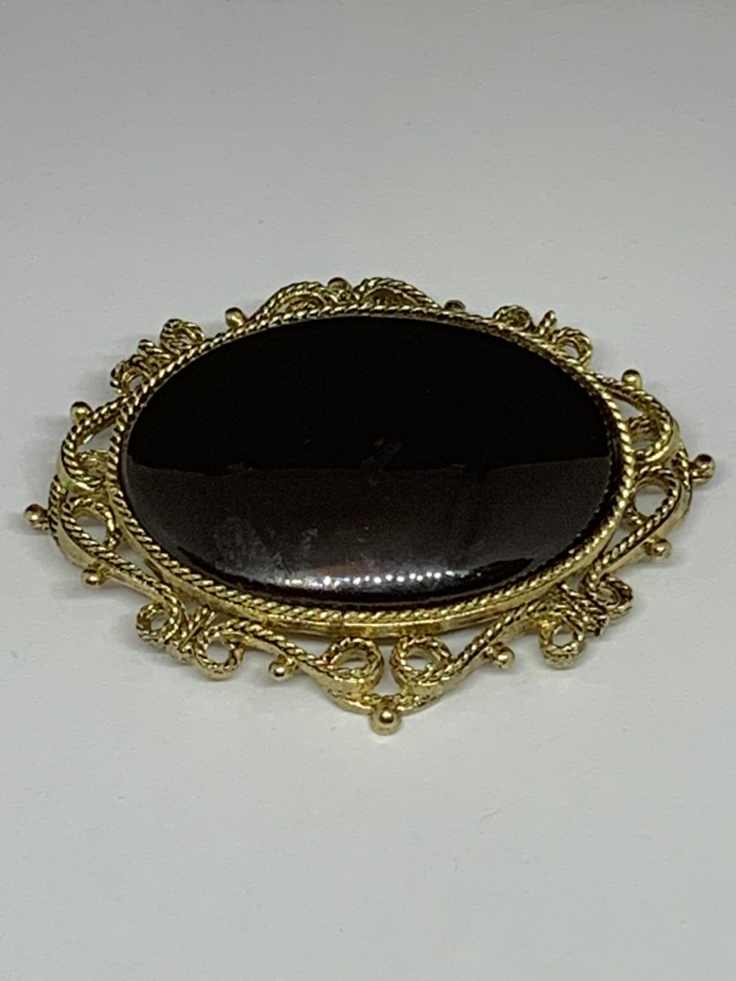 A LARGE BROOCH WITH BLACK STONE WITH ORNATE YELLOW METAL SURROUND MARKED 250 WITH PRESENTATION BAG