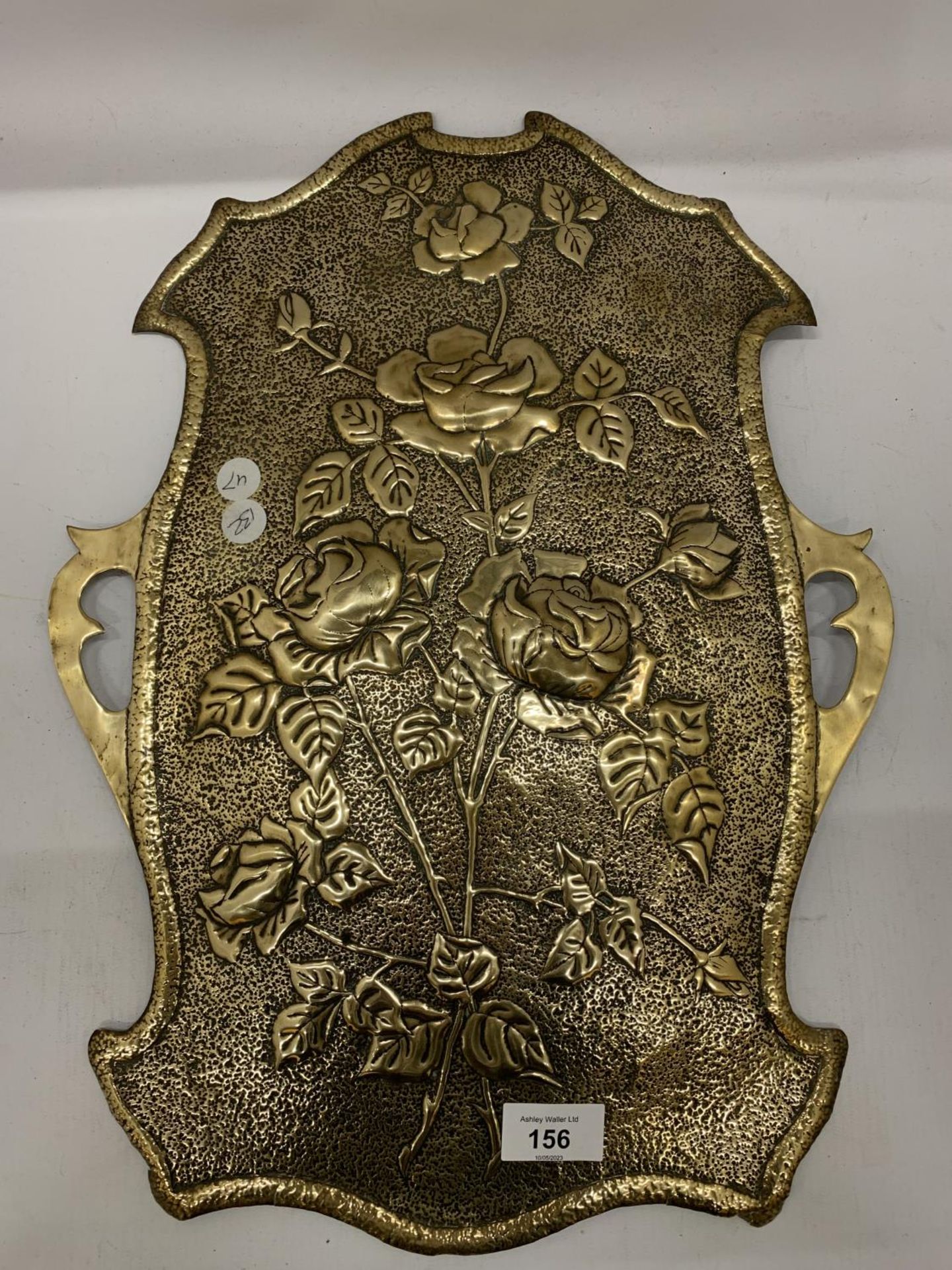 A BRASS WALL HANGING IN THE SHAPE OF A SHIELD WITH FLORAL EMBOSSING 46CM X 34CM