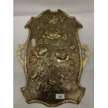 A BRASS WALL HANGING IN THE SHAPE OF A SHIELD WITH FLORAL EMBOSSING 46CM X 34CM