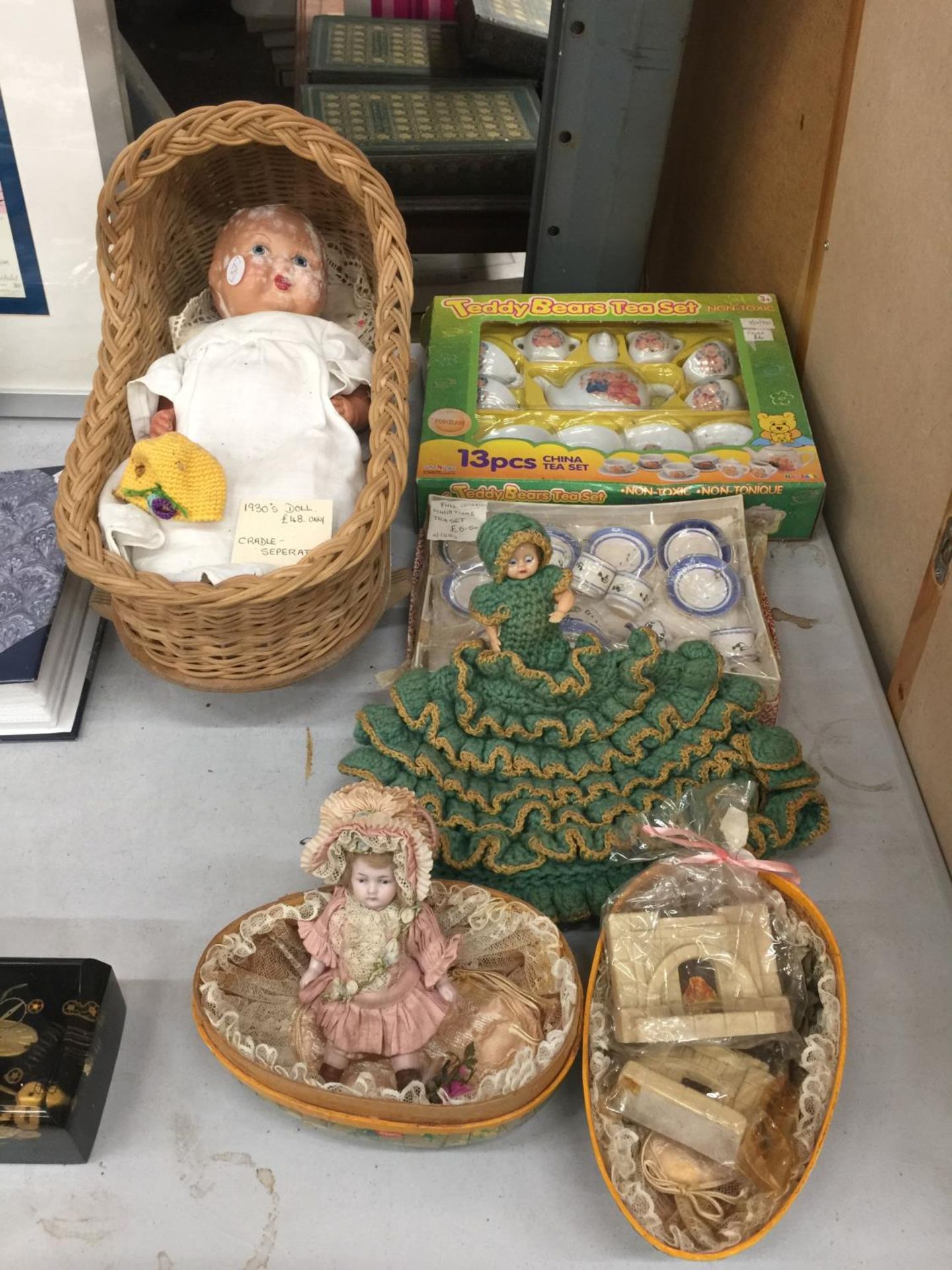 A VINTAGE 1930'S DOLL WITH WICKER CRADLE, TWO SMALLER DOLLS, A BOXED TEDDY BEARS TEA SET, A