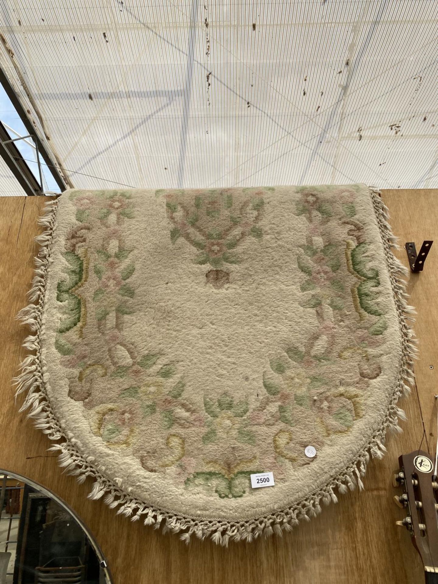 A SMALL OVAL CREAM PATTERNED FRINGED RUG