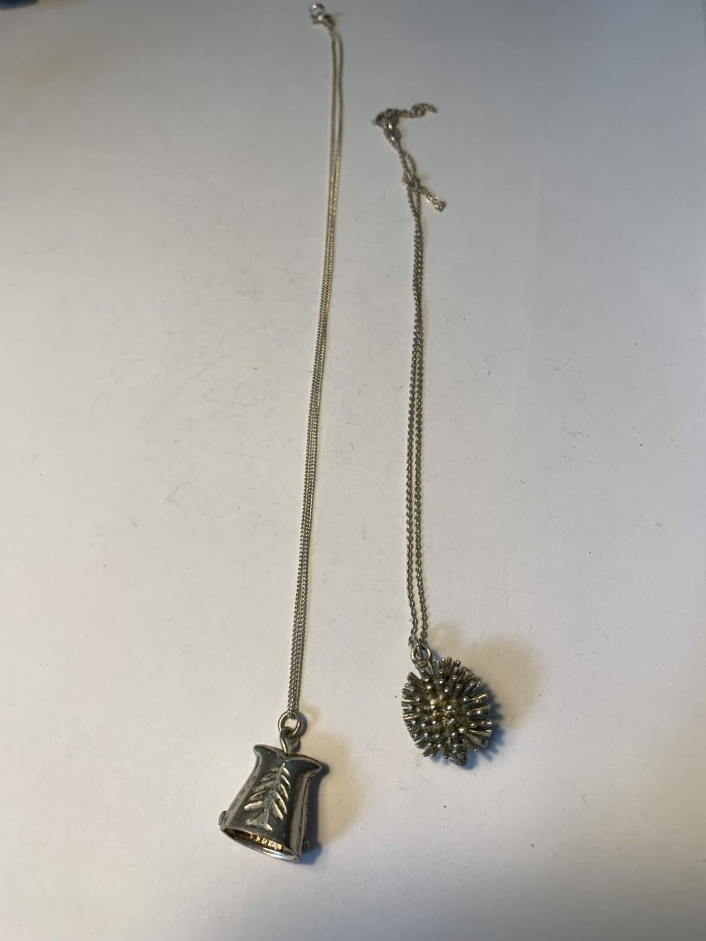 TWO SILVER NECLACES WITH PENDANTS TO INCLUDE A HEDGEHOG AND A BELL