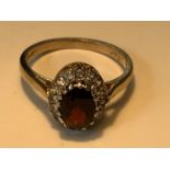 A 9 CARAT GOLD RING WITH A CENTRE RED GARNET SURROUNDED BY CUBIC ZIRCONIAS SIZE K/K