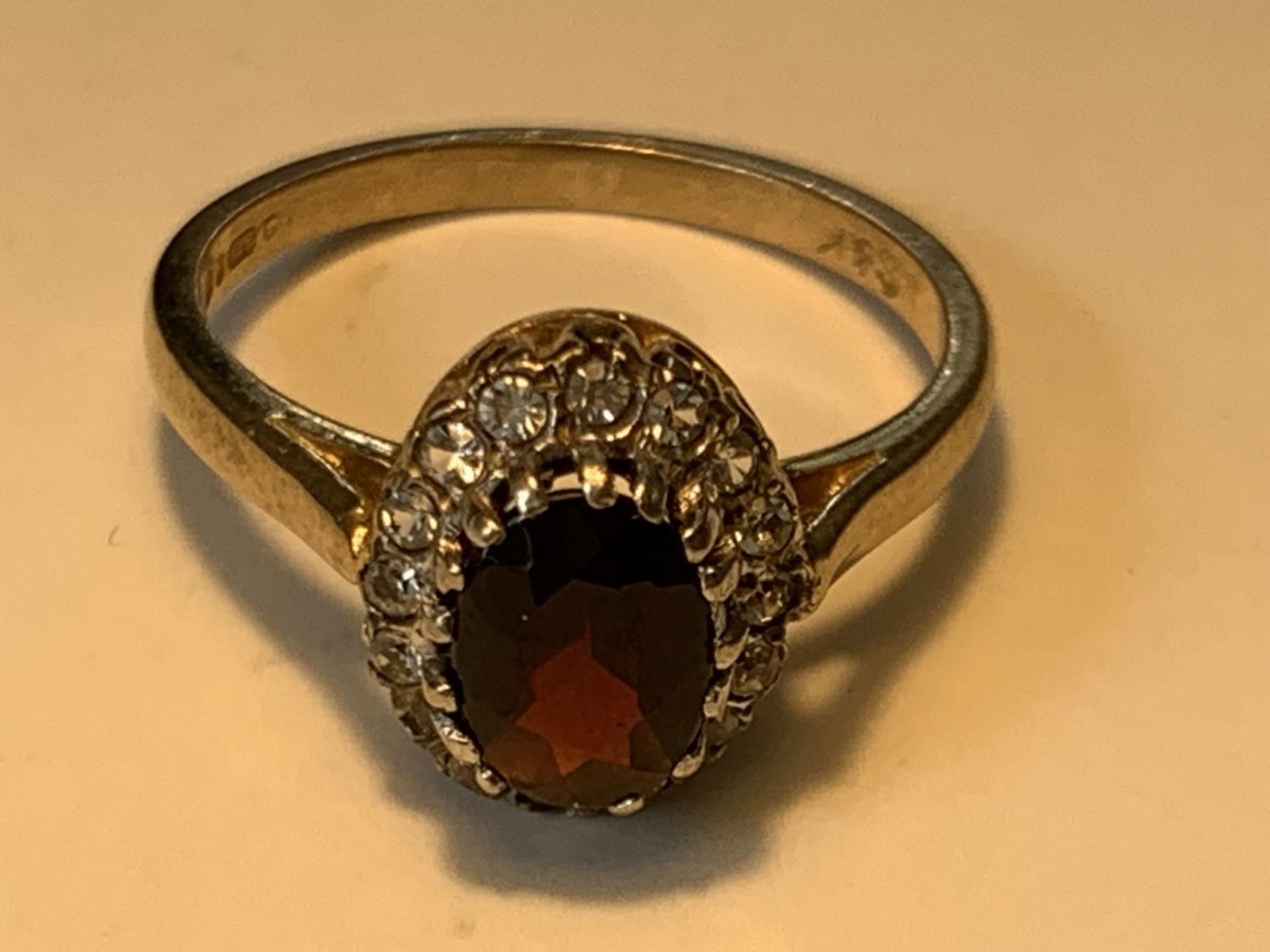 A 9 CARAT GOLD RING WITH A CENTRE RED GARNET SURROUNDED BY CUBIC ZIRCONIAS SIZE K/K