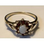 A 9 CARAT GOLD RING WITH A CENTRE OPAL SURROUNDED BY EIGHT GARNETS SIZE O GROSS WEIGHT 1.73 GRAMS