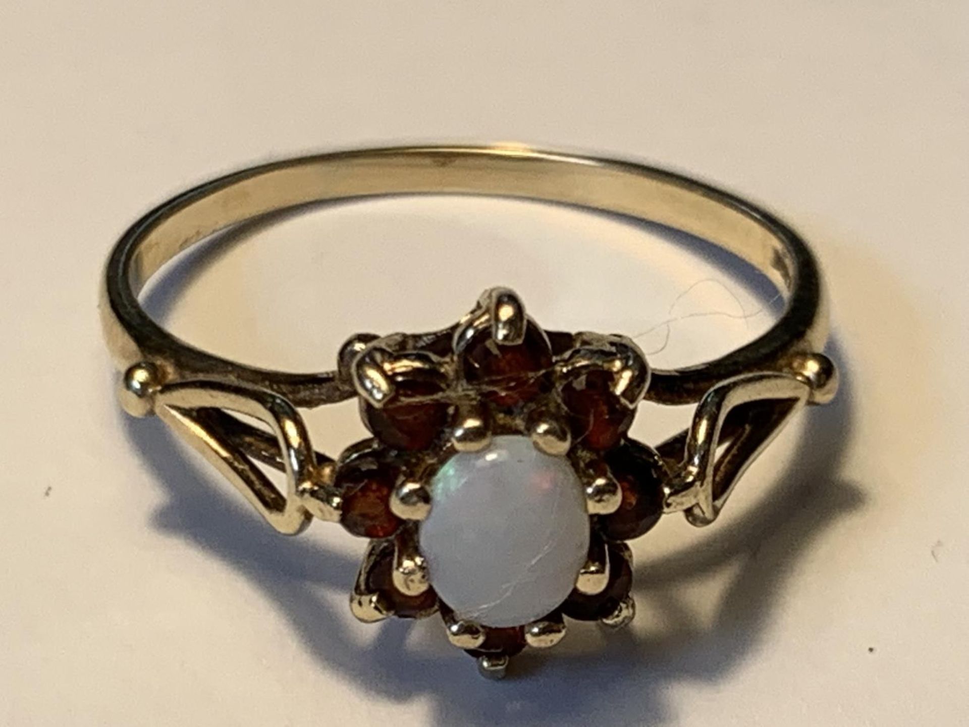 A 9 CARAT GOLD RING WITH A CENTRE OPAL SURROUNDED BY EIGHT GARNETS SIZE O GROSS WEIGHT 1.73 GRAMS