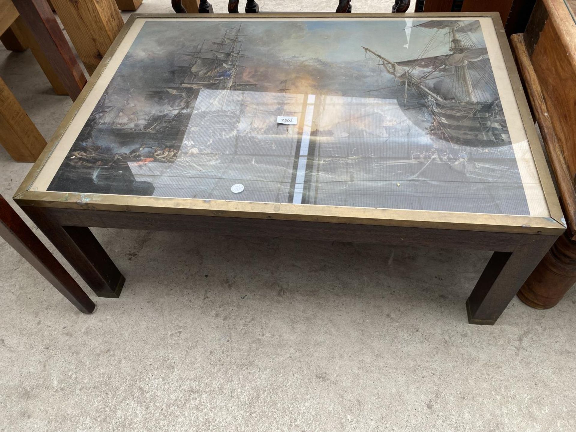 A MODERN COFFEE TABLE WITH BRASS TRIM, THE TOP DEPICTING MASTED BATTLESHIPS, 35X24"
