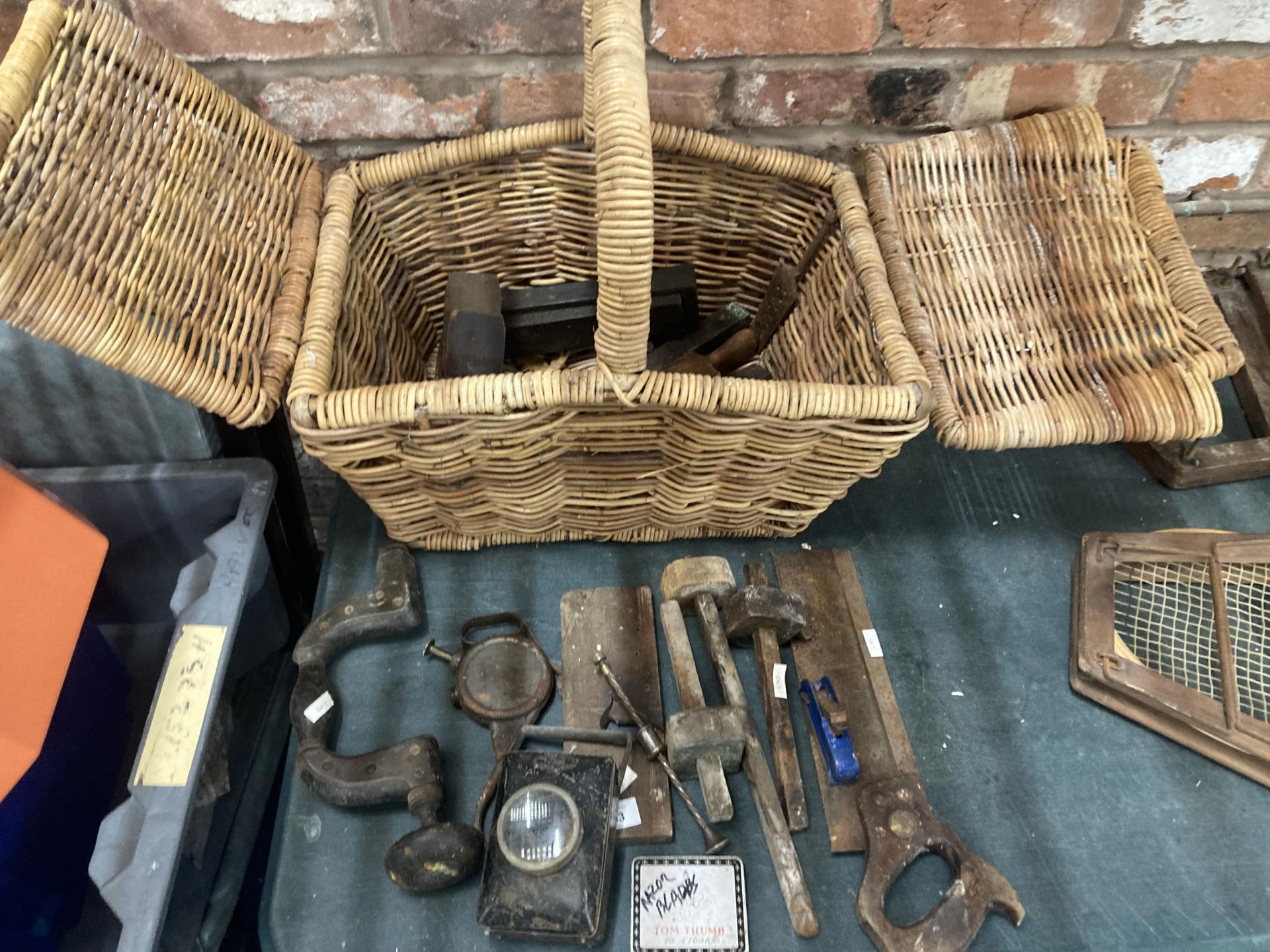 A WICKER BASKET CONTAINING A QUANTITY OF VINTAGE TOOLS TO INCLUDE WOODEN MALLETS, PLANES, A LAMP,